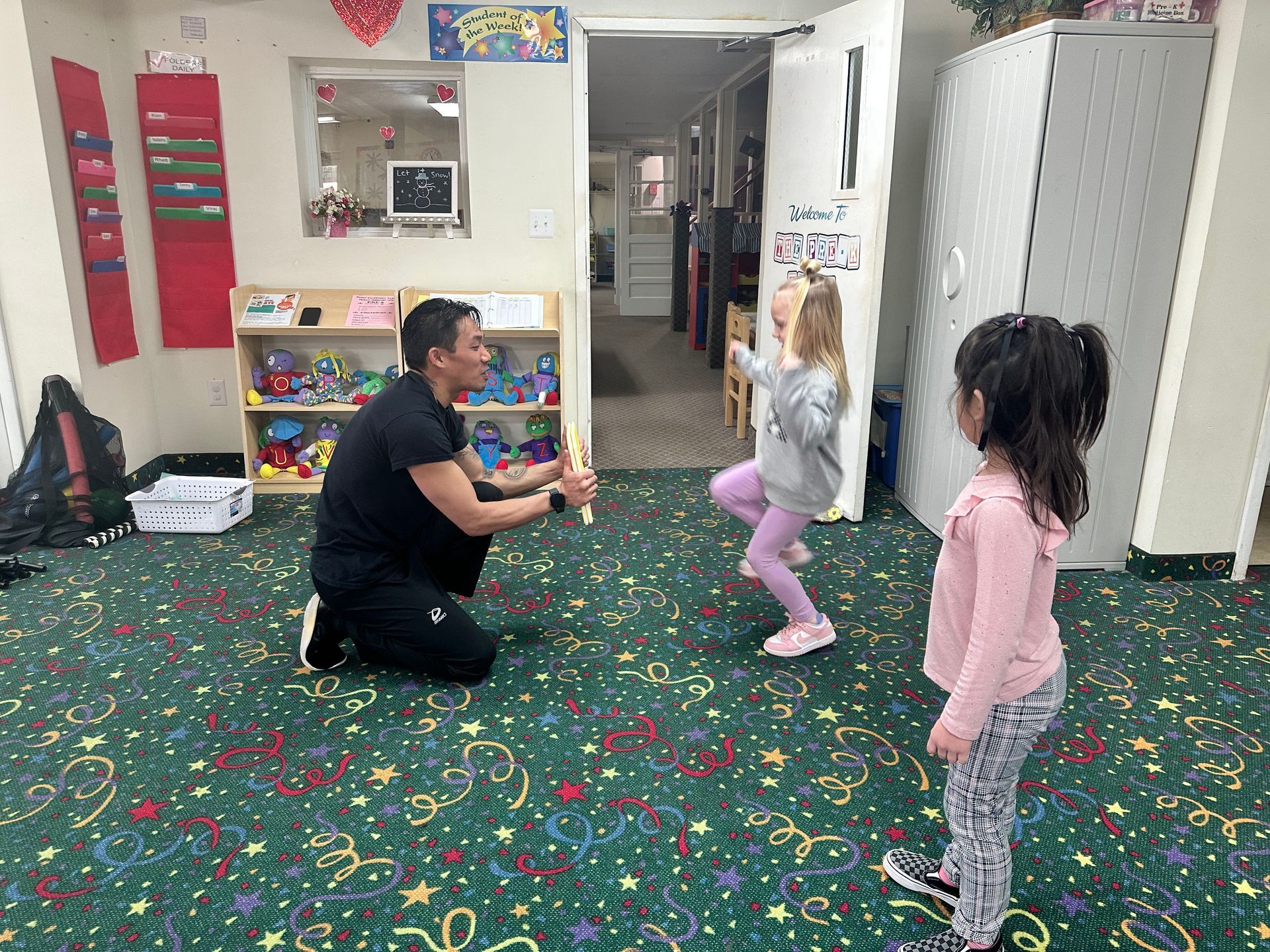 A man is kneeling down in a room with two little girls.