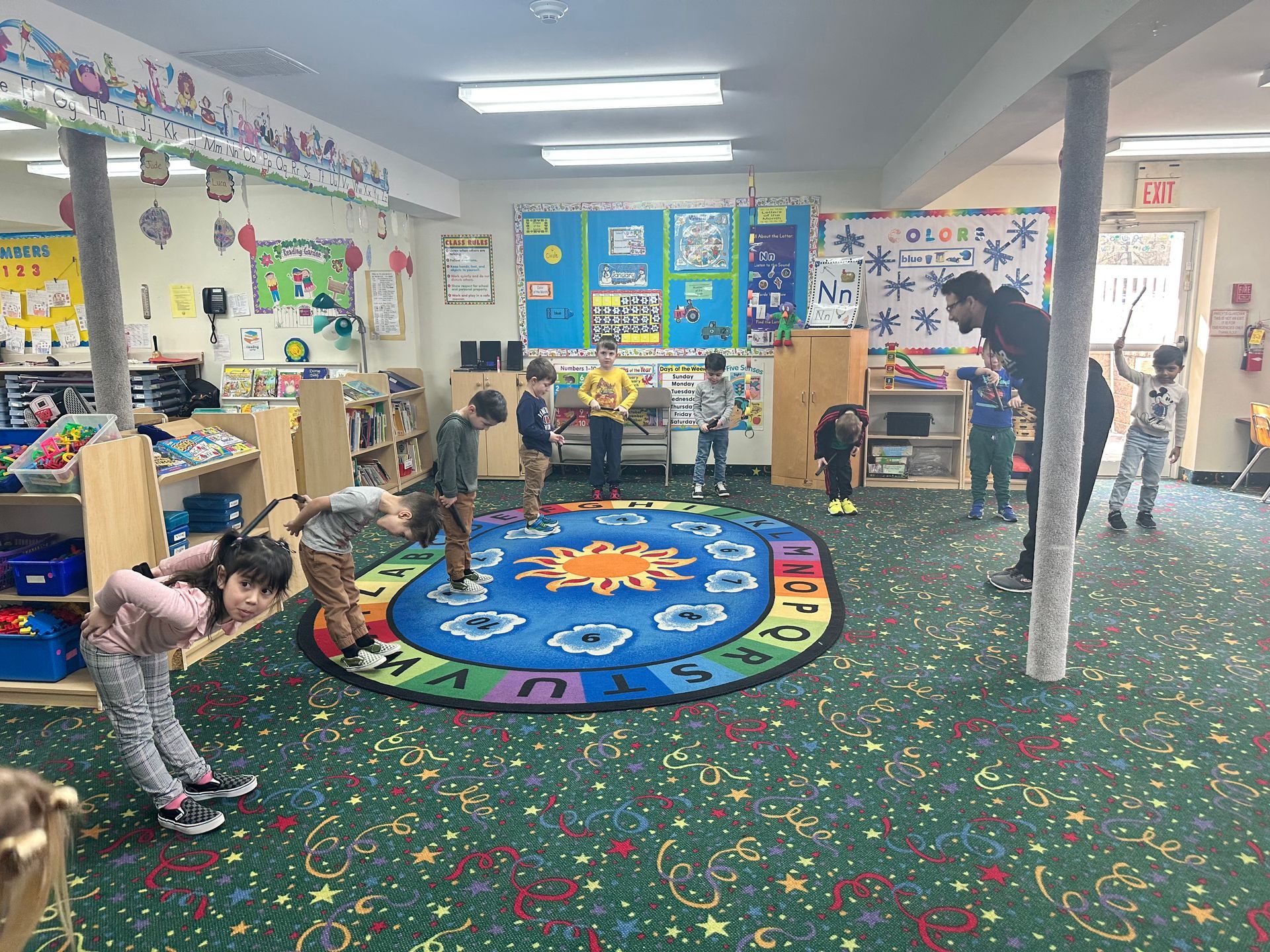A group of children are playing in a classroom with a colorful rug.
