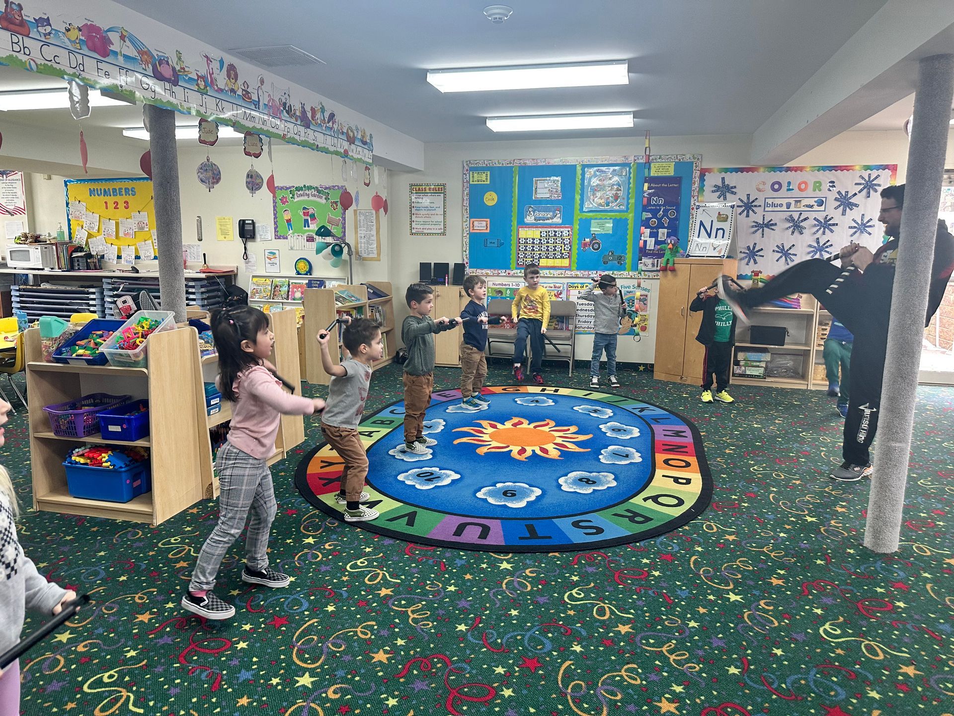 A group of children are standing around a rug in a classroom.