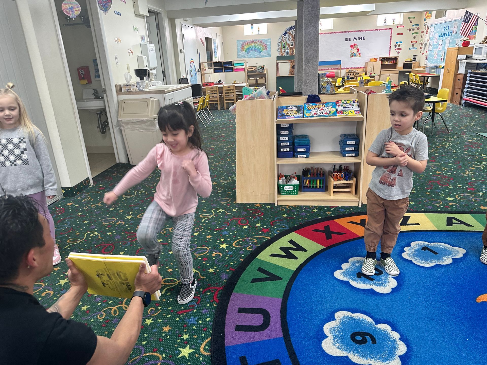 A man is reading a book to two children in a classroom.