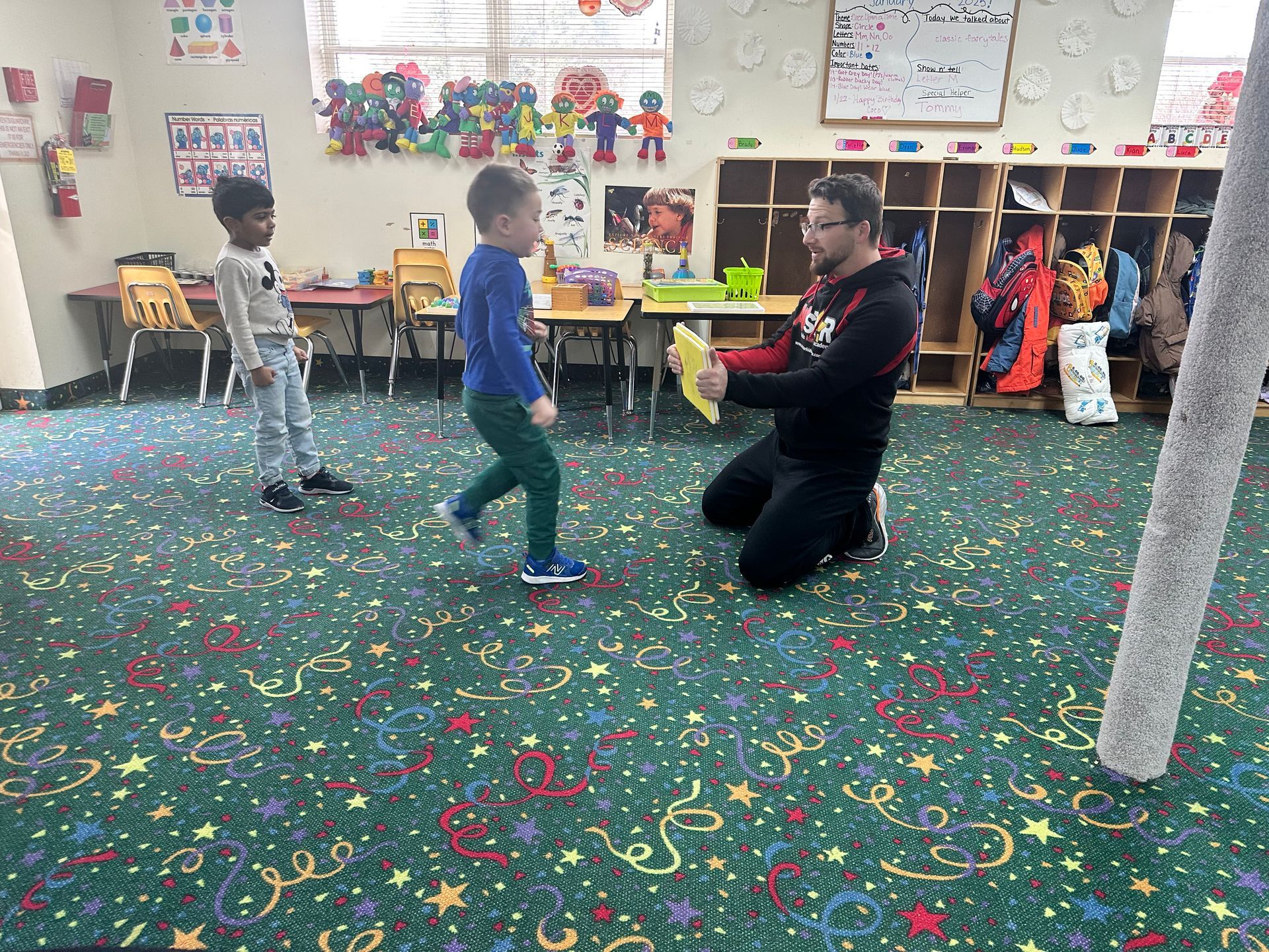A man is kneeling down in a classroom with two children.