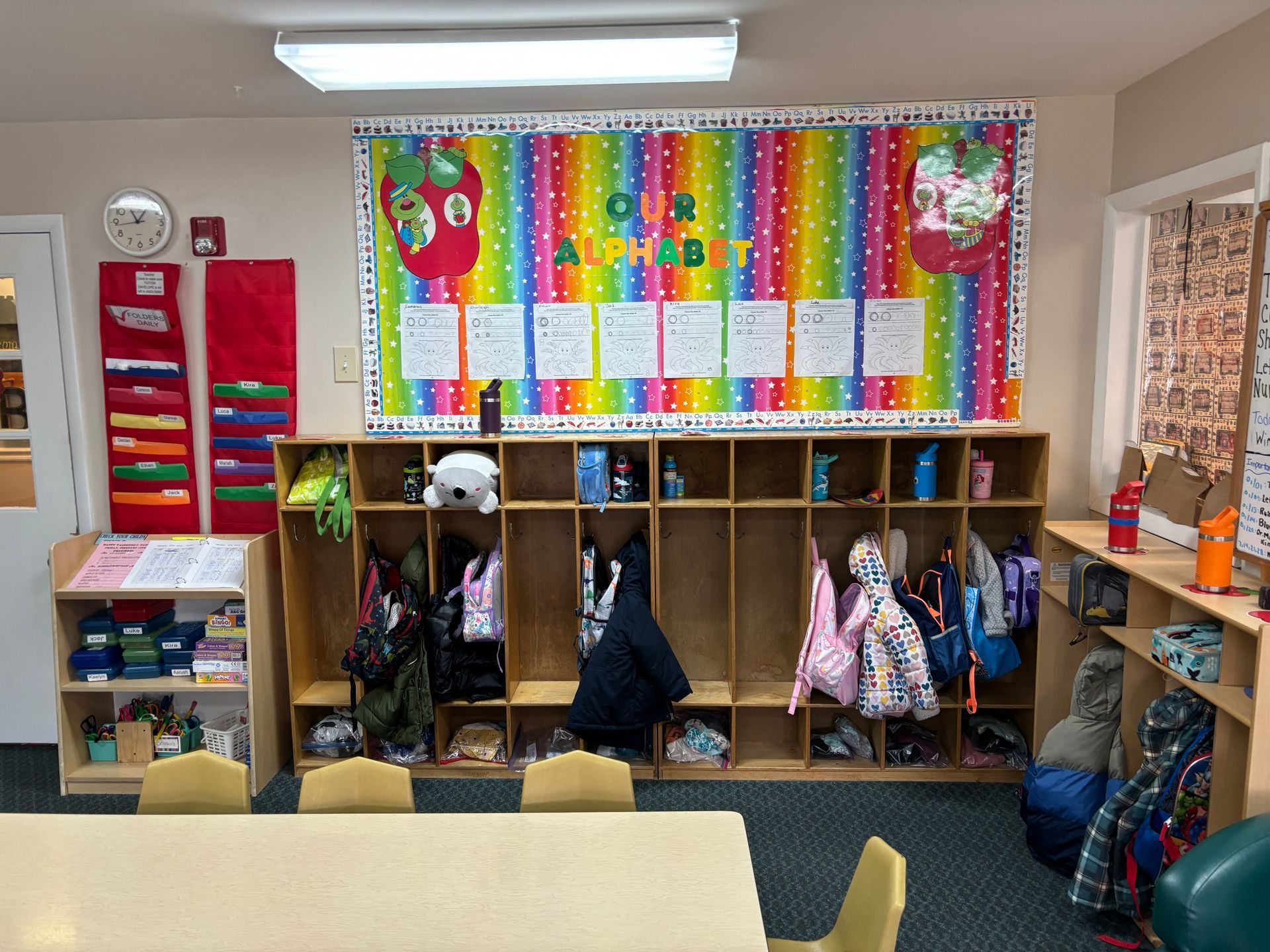 A classroom with a rainbow bulletin board and a table and chairs.