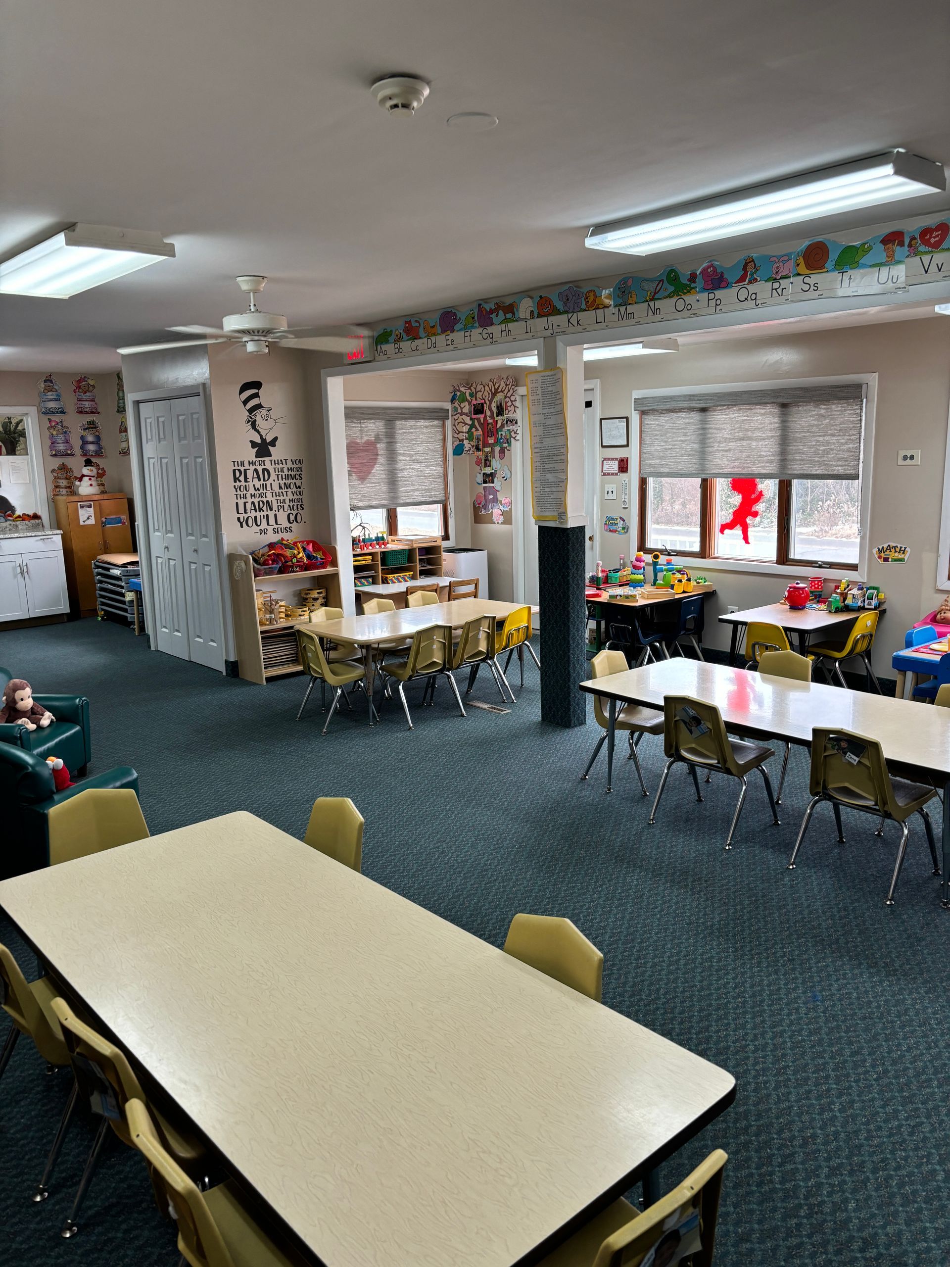 A classroom with tables and chairs and a baby in a chair.