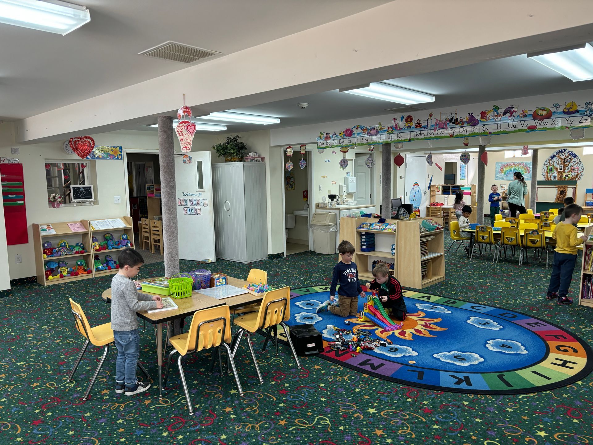 A group of children are playing in a classroom with tables and chairs.