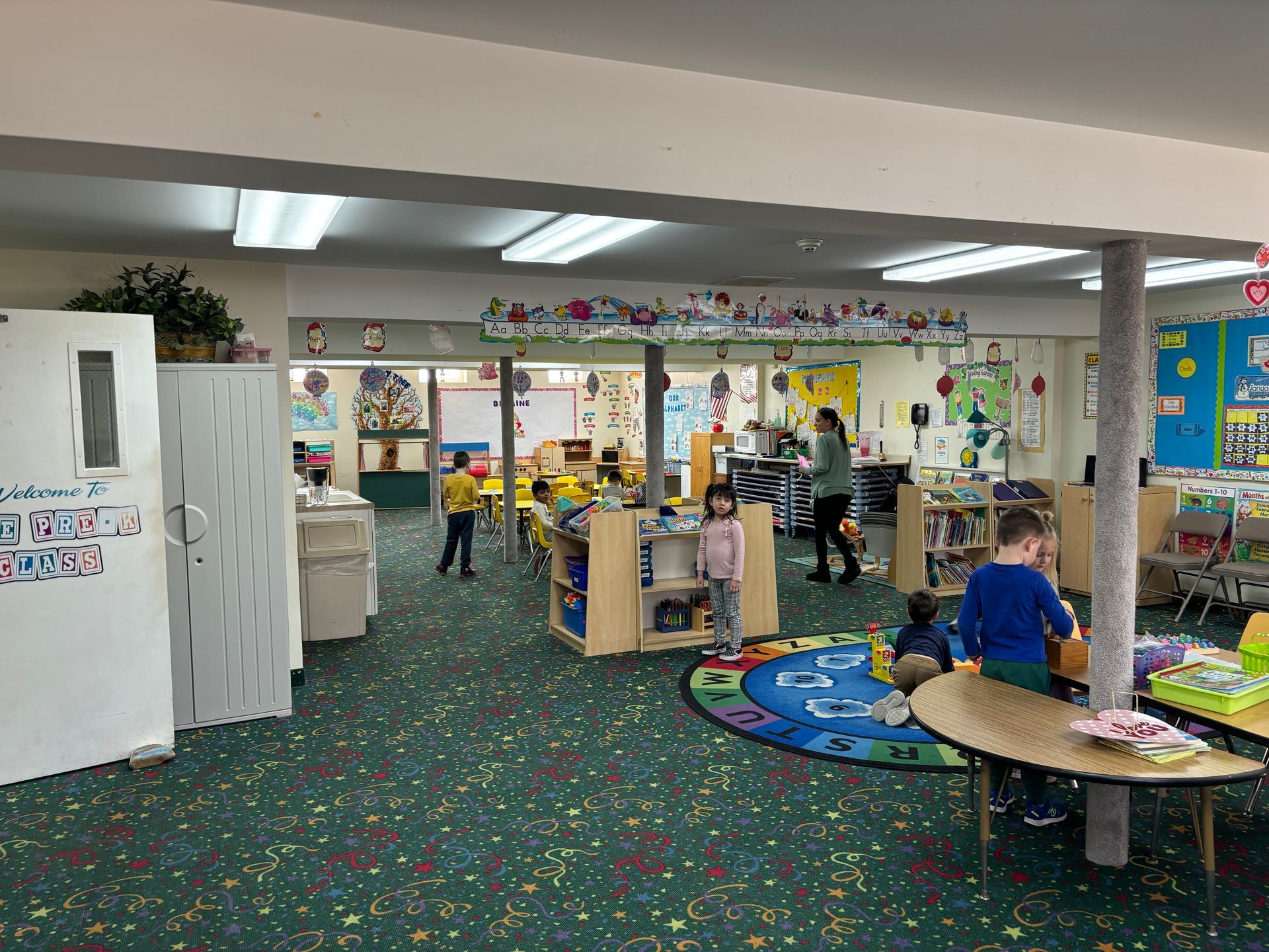 A group of children are playing in a classroom with tables and chairs.