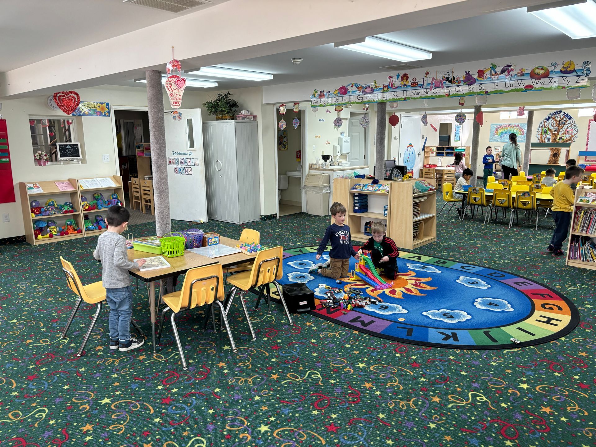 A group of children are playing in a classroom with tables and chairs.