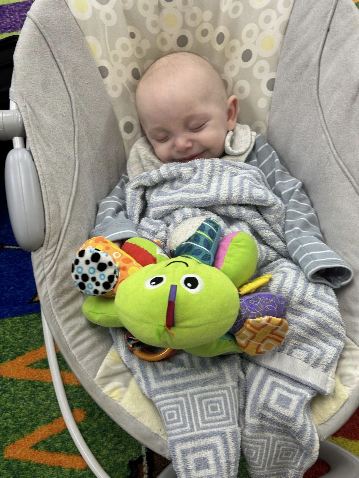 Baby asleep in a gray swing, wrapped in a matching blanket