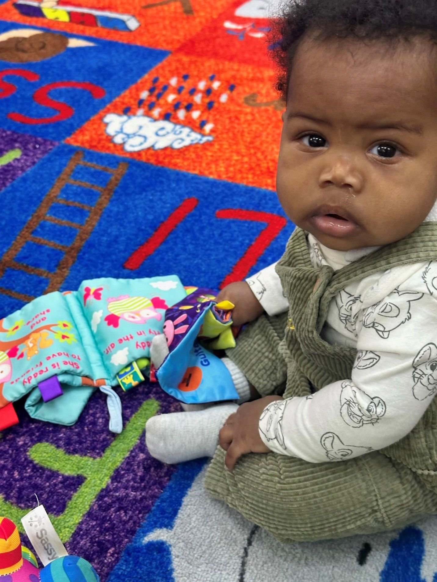 Baby sitting on a colorful rug, looking at the viewer
