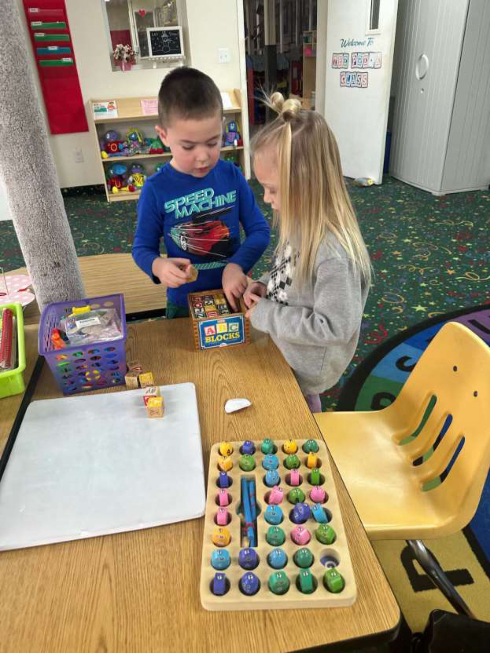 Two young children at a table playing with educational toys in a classroom.