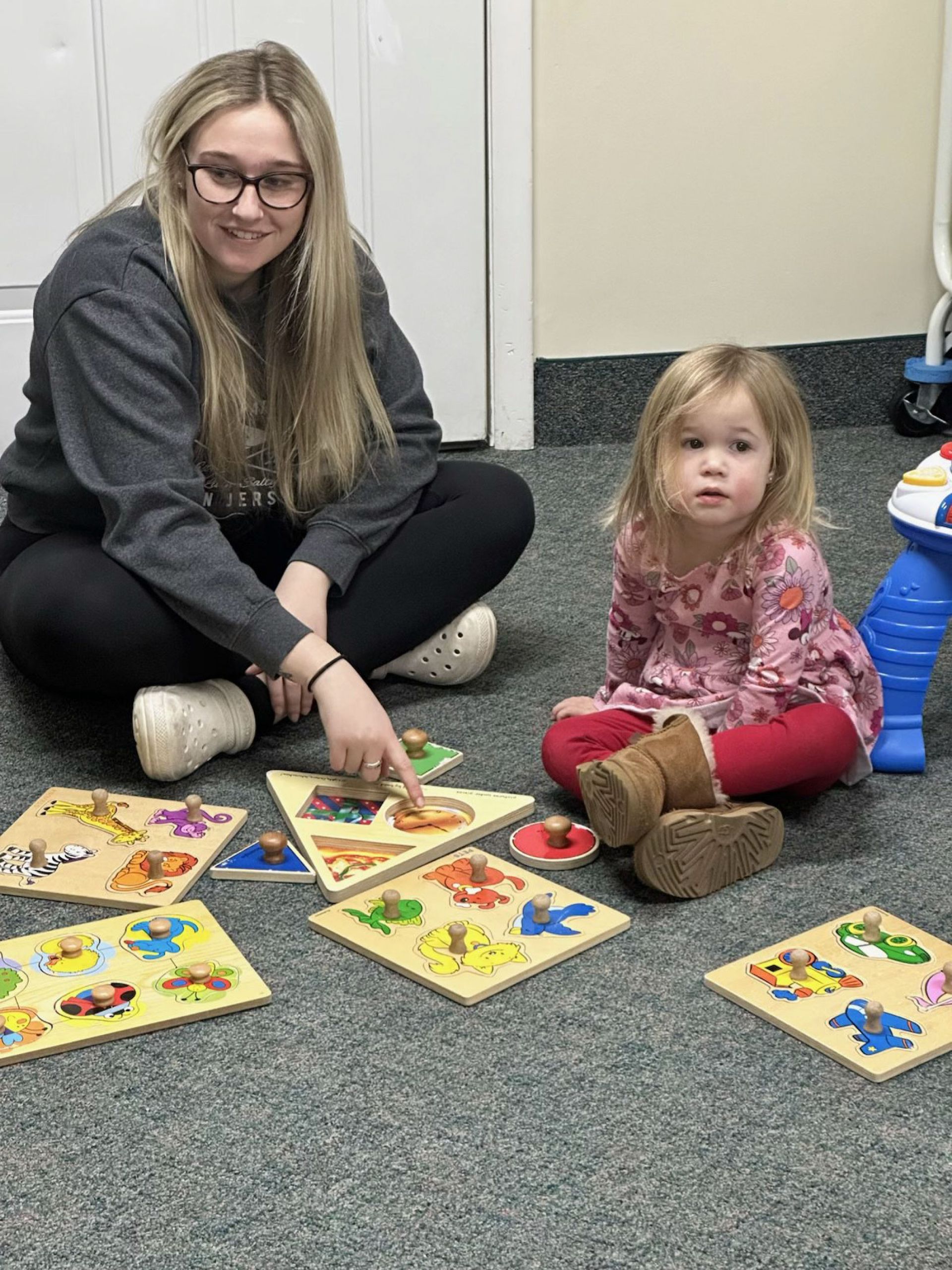 Woman and young child playing with wooden puzzles on a carpeted floor