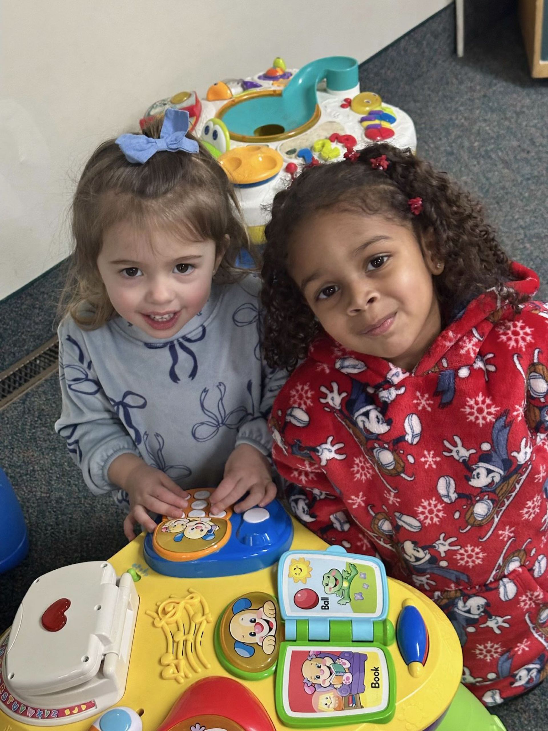 Two young girls smiling, playing with a colorful activity center