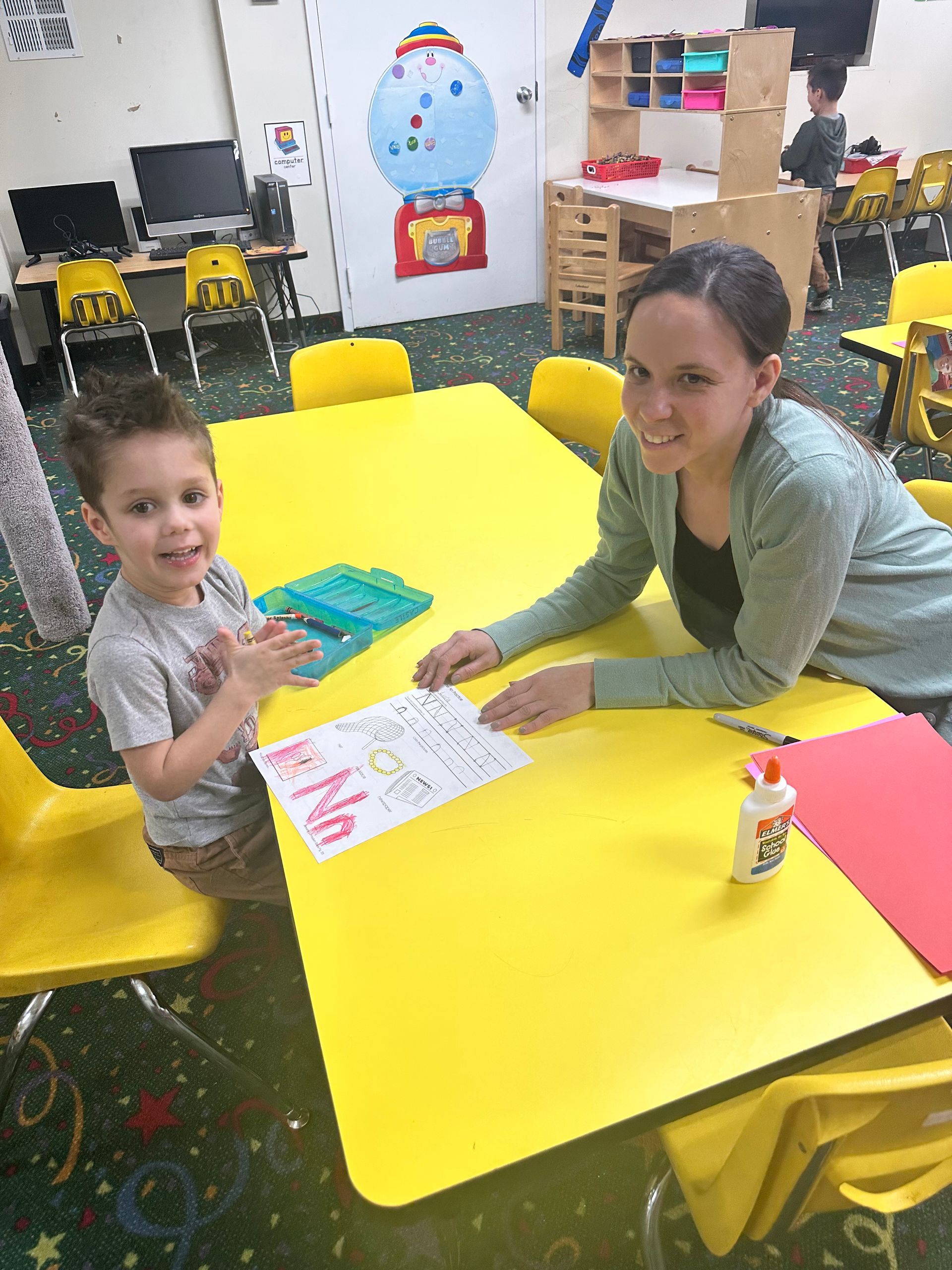 A group of children are sitting around a table with a woman standing behind them.