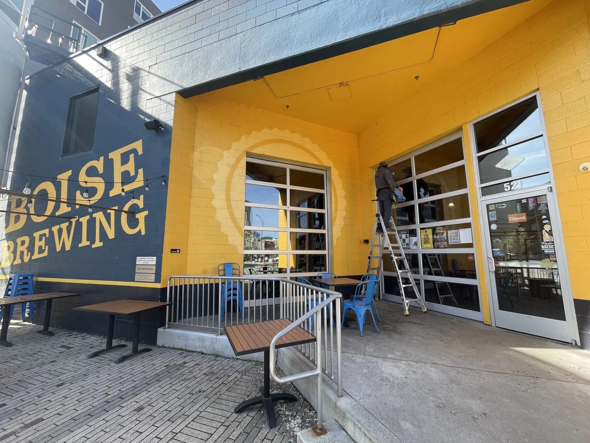 Boise Brewing exterior: yellow building with glass doors, outdoor seating, and a ladder leaning against the side.