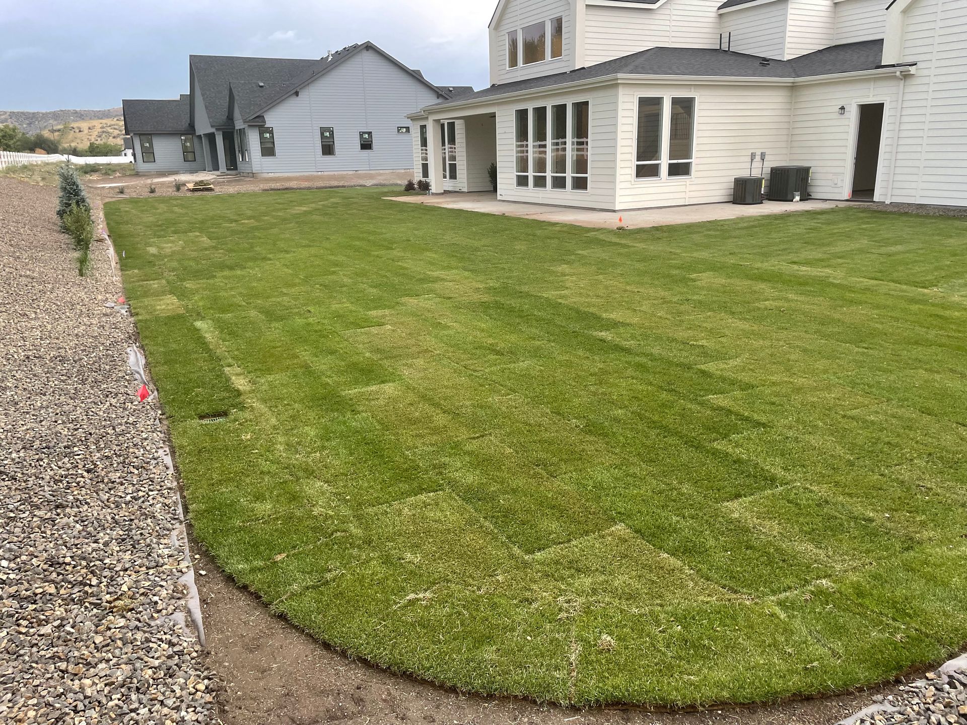 Newly sodded green lawn in backyard, bordering a gravel bed and white house.