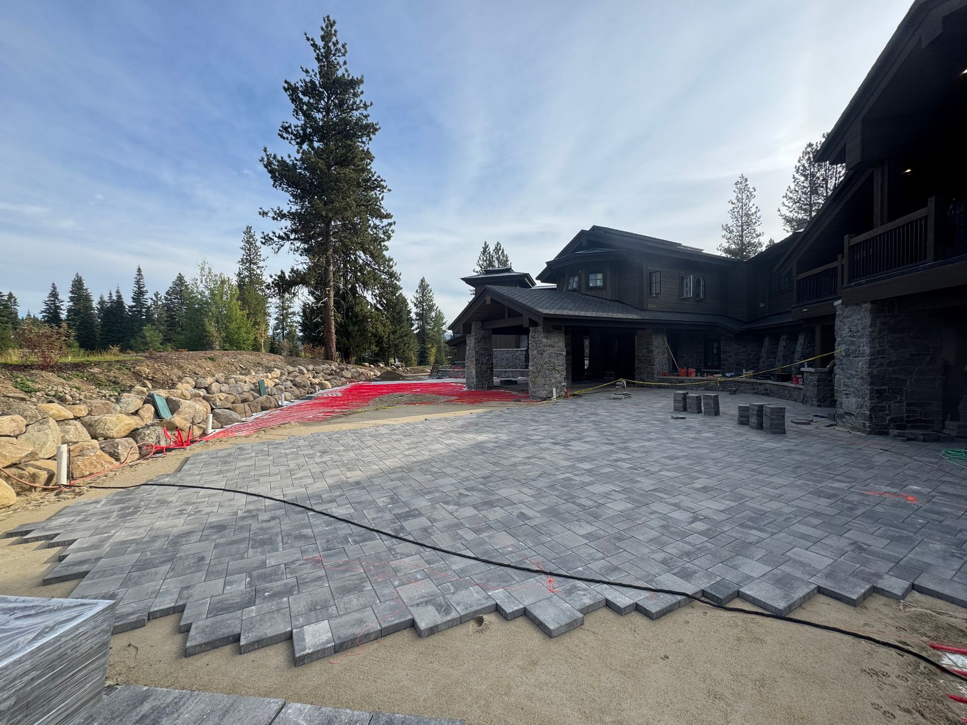 Exterior patio under construction with stone pavers in front of a dark wood house.