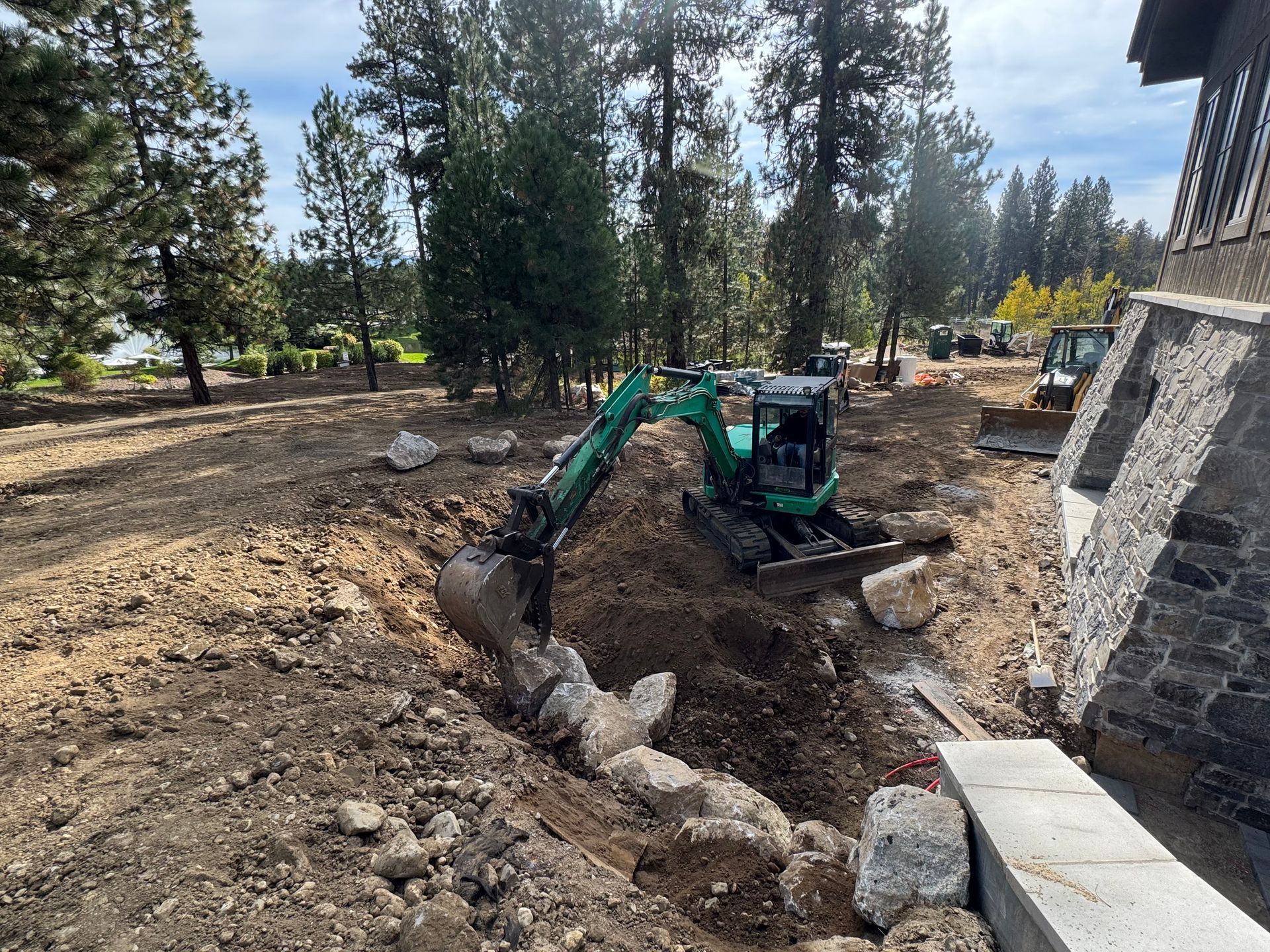 Mini excavator digging in dirt near a stone building and trees.