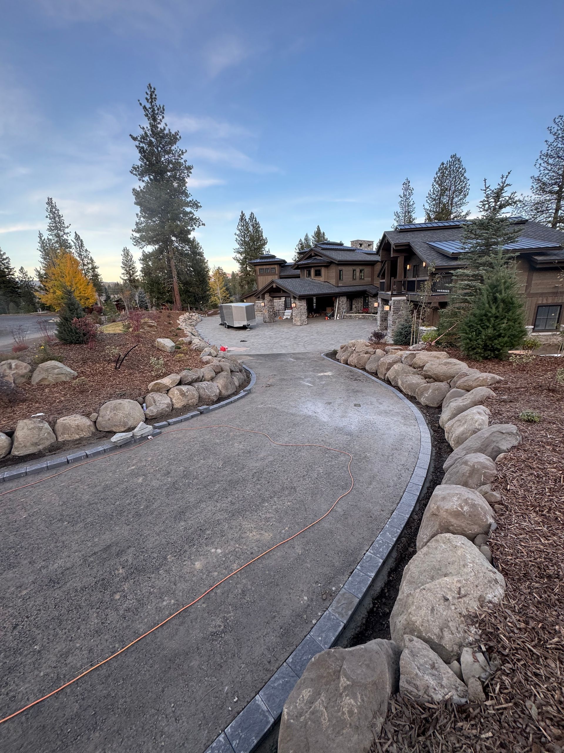 Curved gravel driveway leading to a large house with stone accents, lined by rock and landscaping.