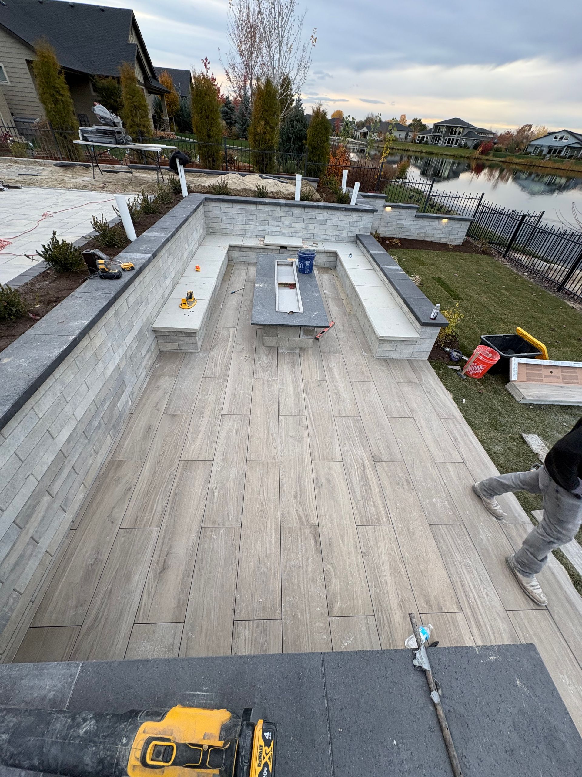 Workers laying stone pavers on a patio with built-in seating. A person walks on the right.