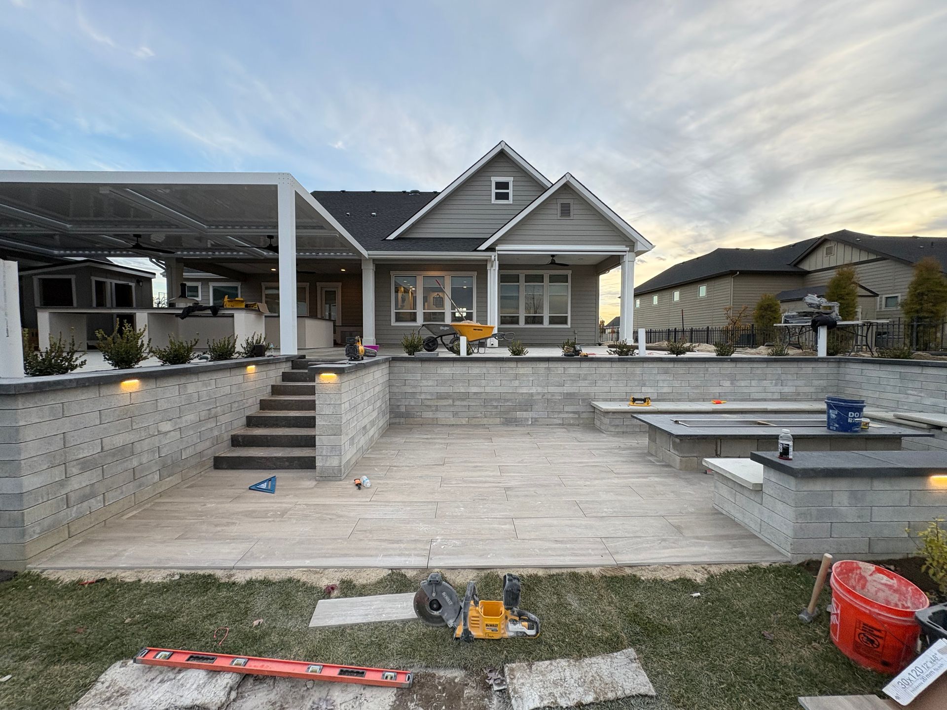 Backyard patio with tiered levels and house in the background; partially constructed, cloudy sky.