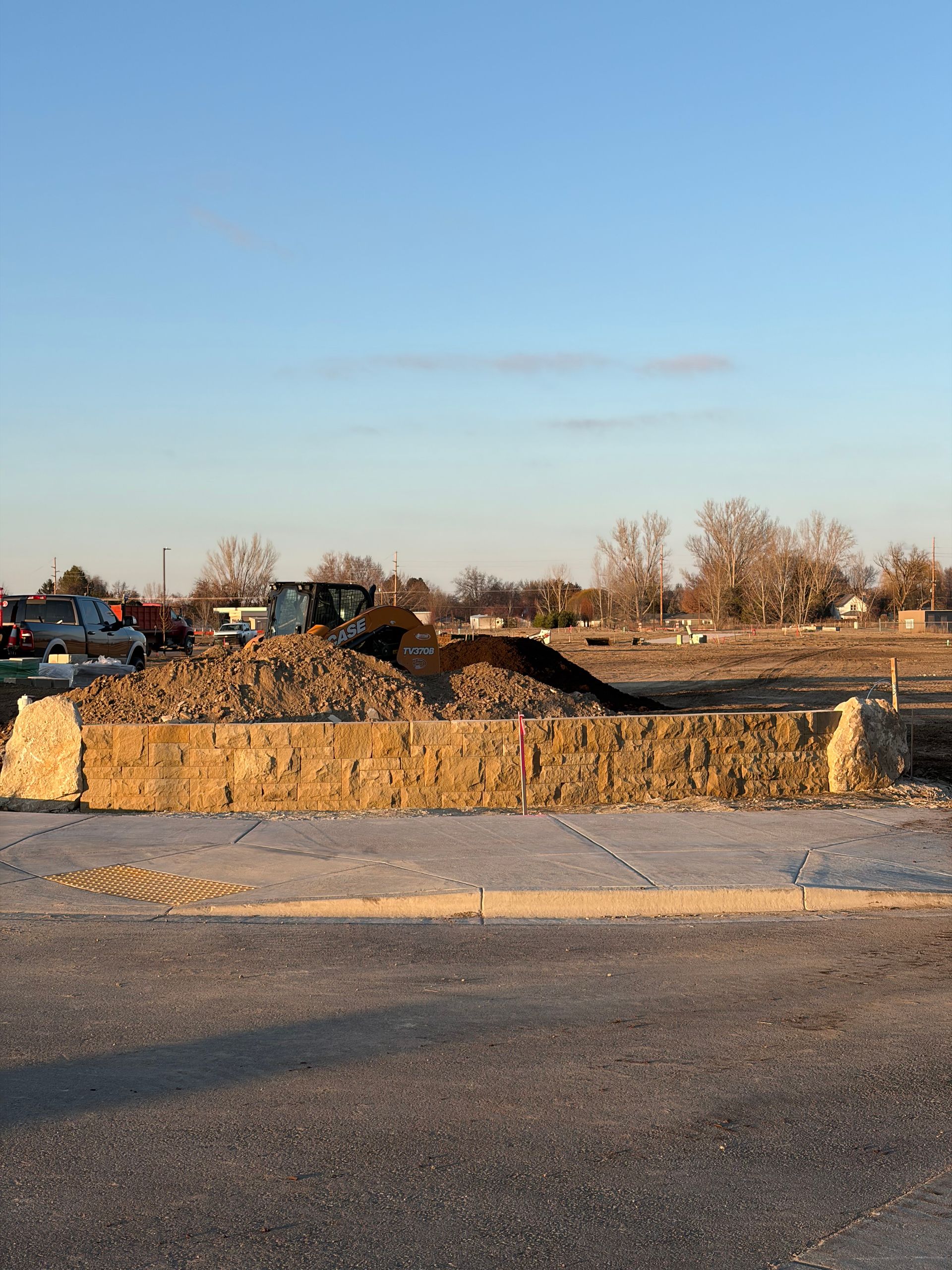 Construction site with pile of dirt and equipment. Road in foreground, blue sky.
