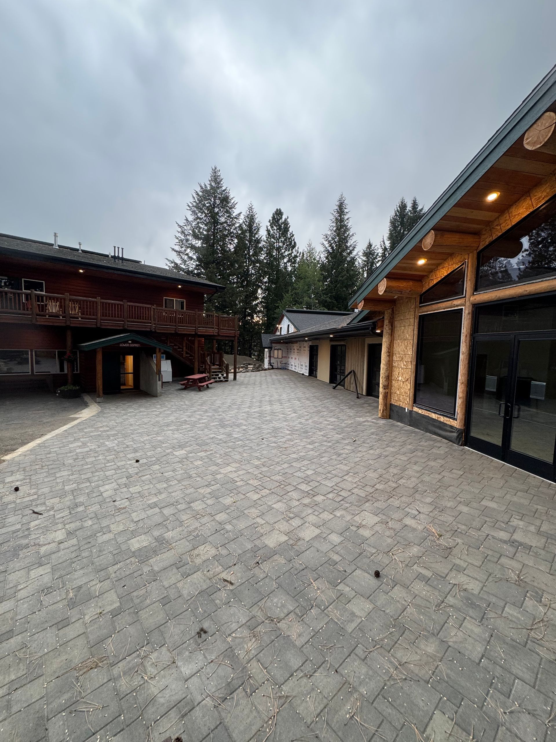 Cobblestone courtyard between wooden buildings, trees in the background under a cloudy sky.