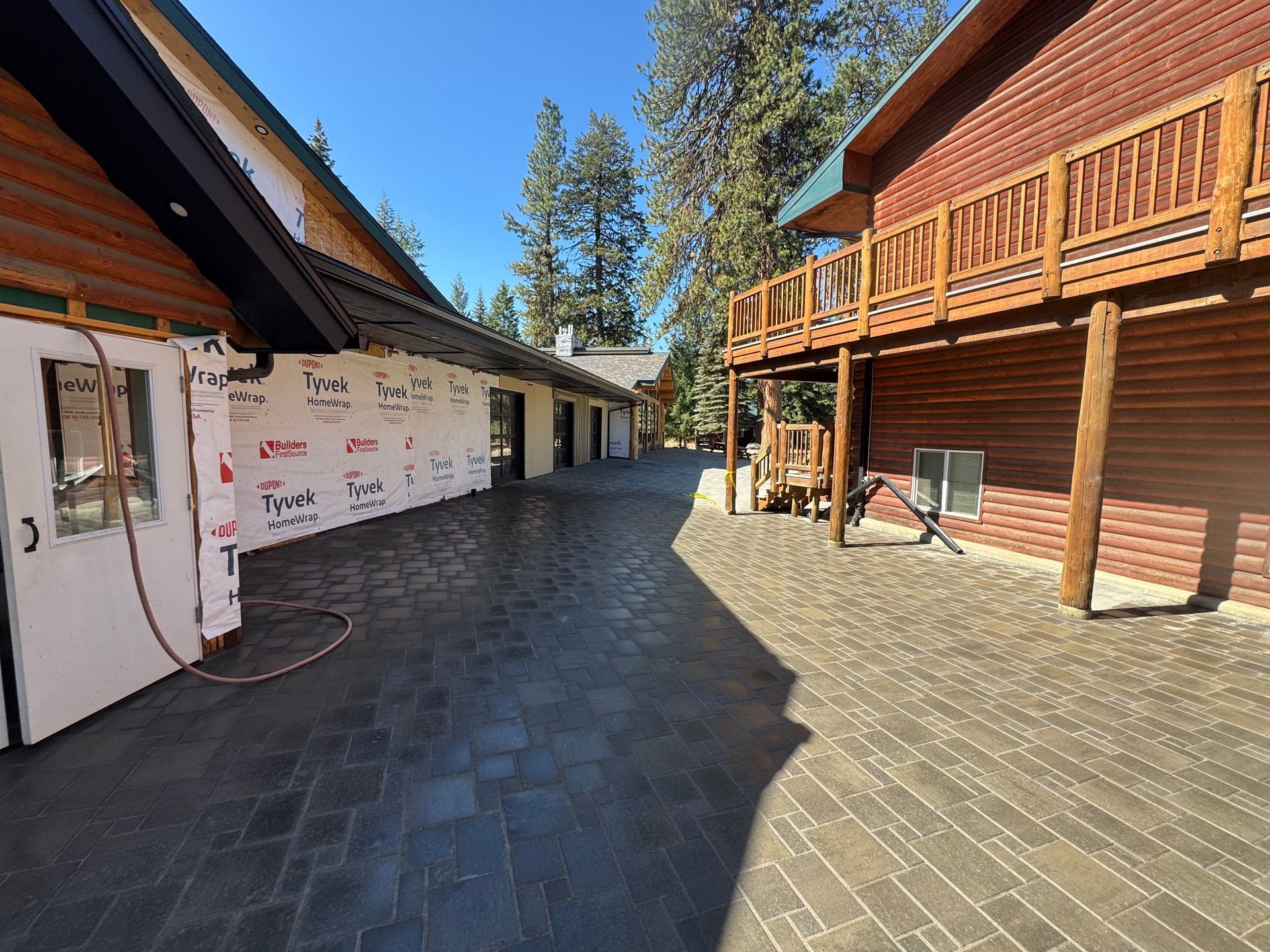 Exterior view of two connected buildings with textured concrete path. One building is log cabin style, other under construction.