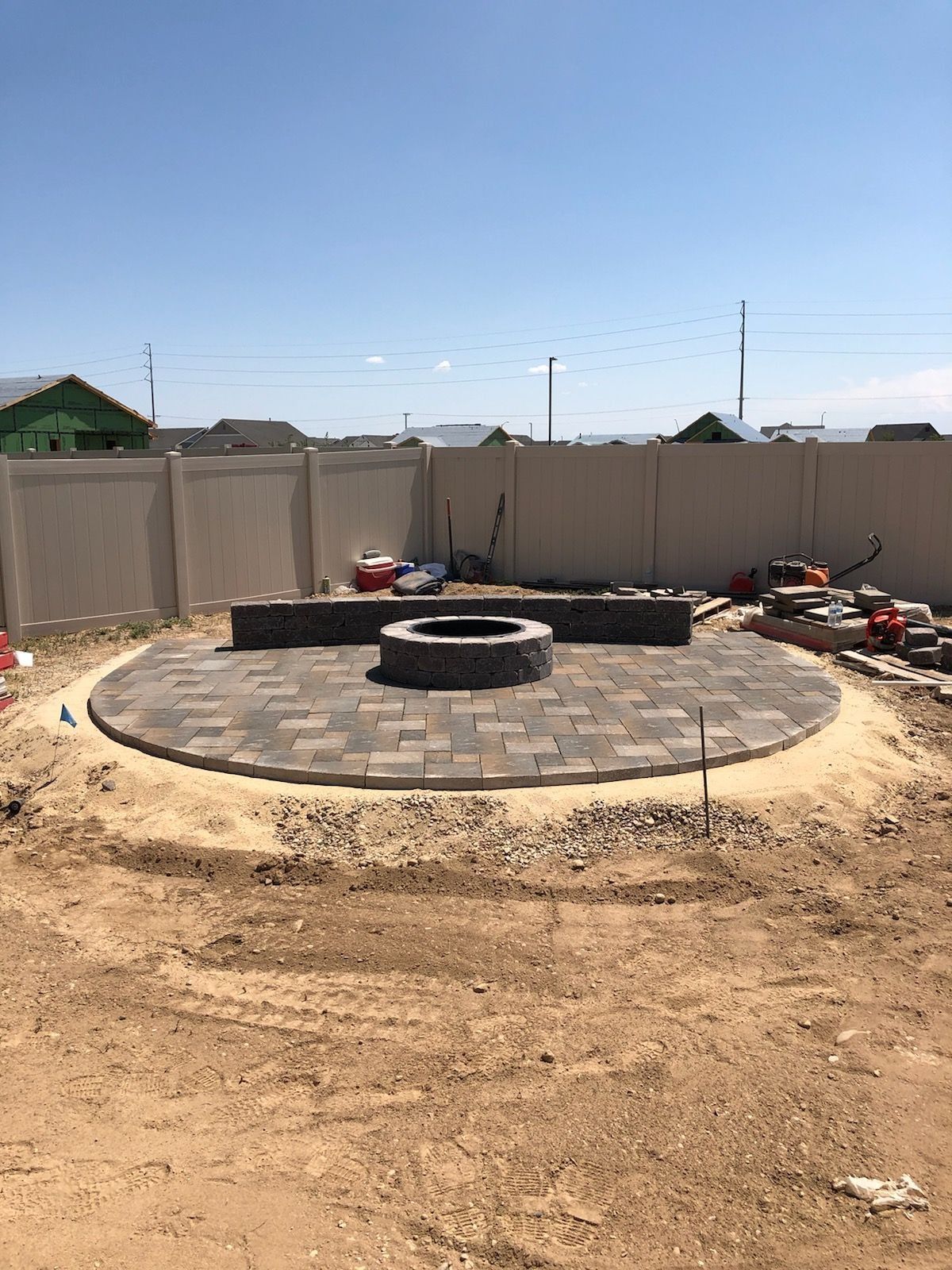Fire pit and patio under construction in a backyard, surrounded by a fence and dirt.
