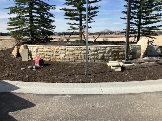 Stone retaining wall with trees, landscaping, and concrete curb.