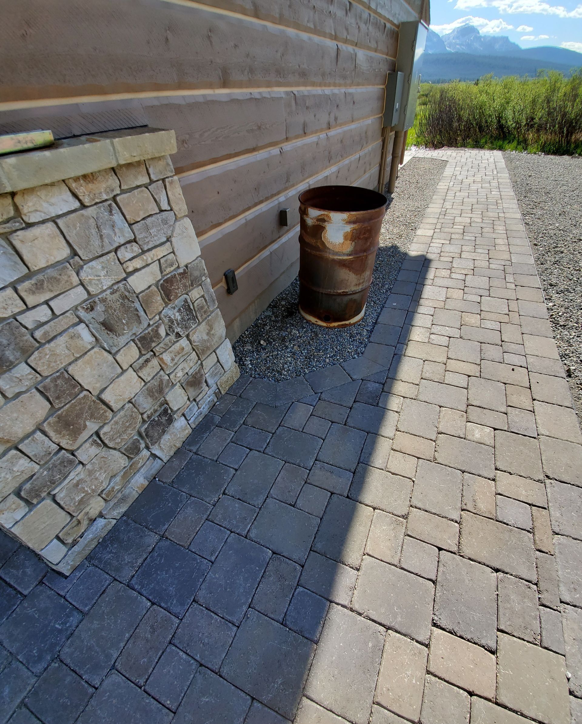 Stone and wood exterior with paved walkway and rusty metal barrel.