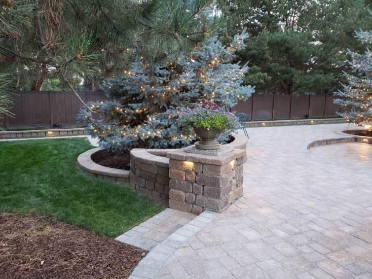 Stone patio and retaining wall with evergreen tree decorated with lights.