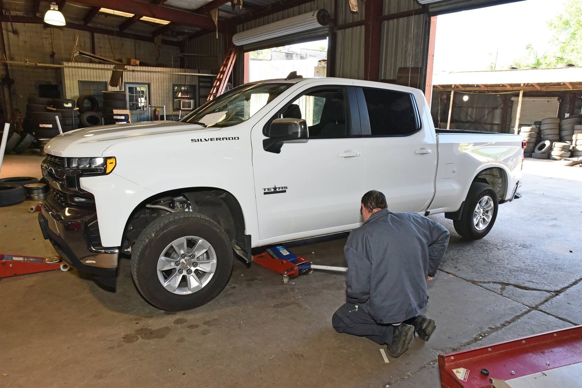 White pickup truck in a garage while a mechanic kneels by the front wheel on a lift