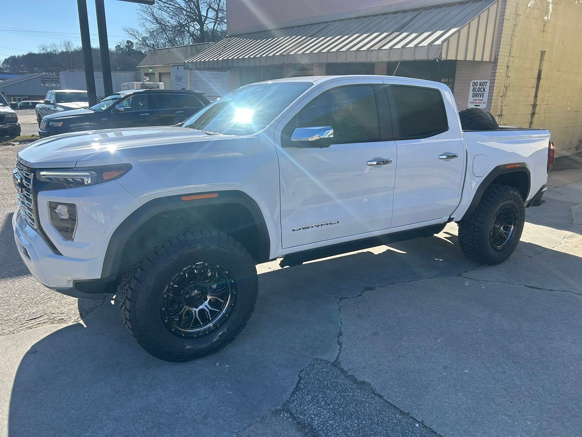White lifted pickup truck parked outside a building in bright sunlight