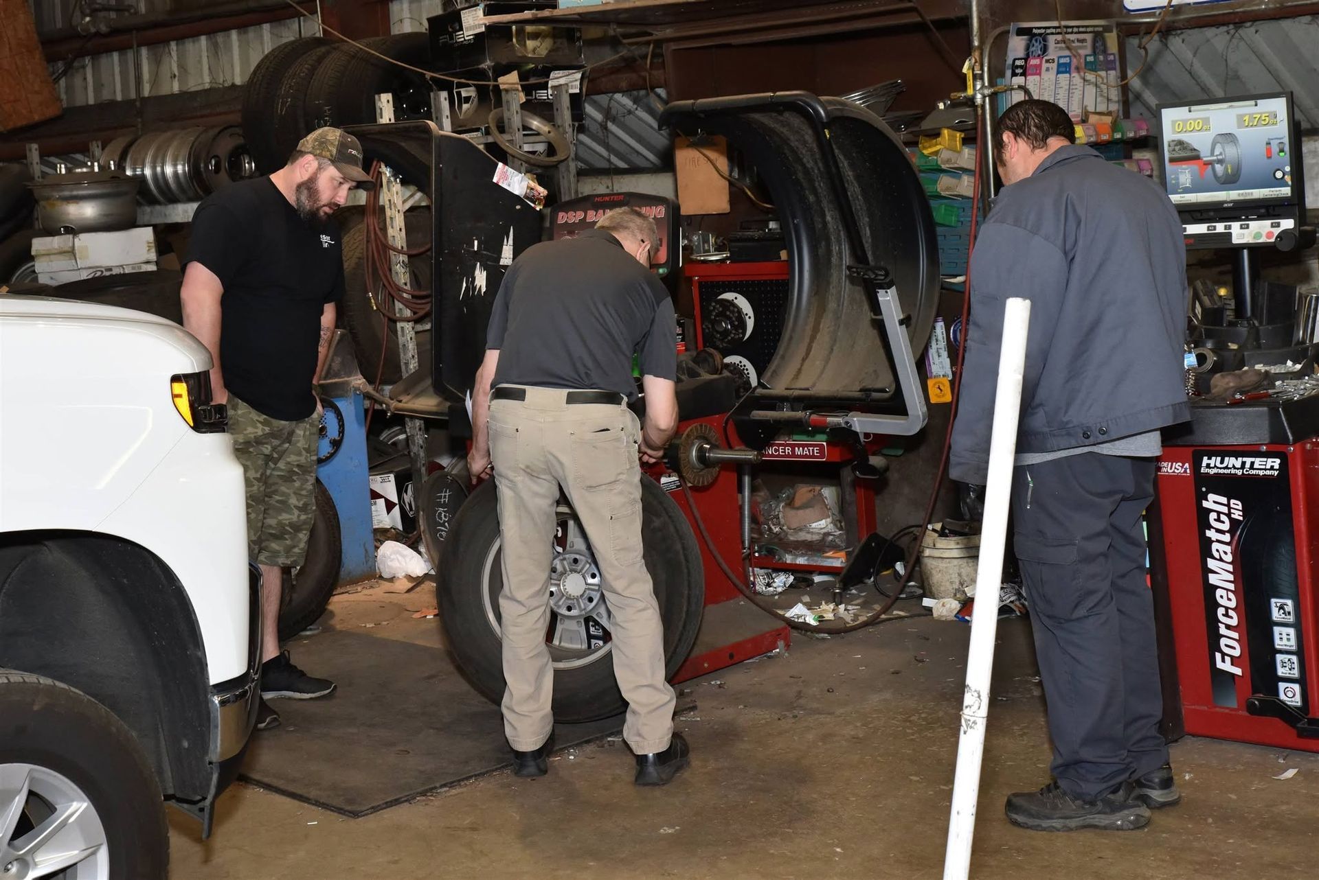 Mechanics working on an SUV with its hood open inside a cluttered auto shop