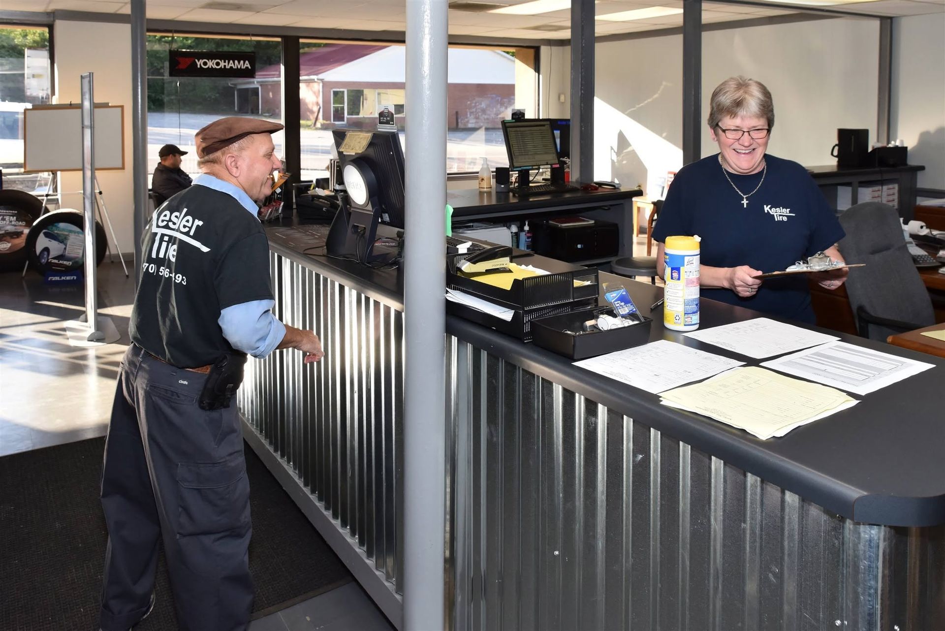 Customer and staff member at a service counter in a public office, with papers and computers nearby.