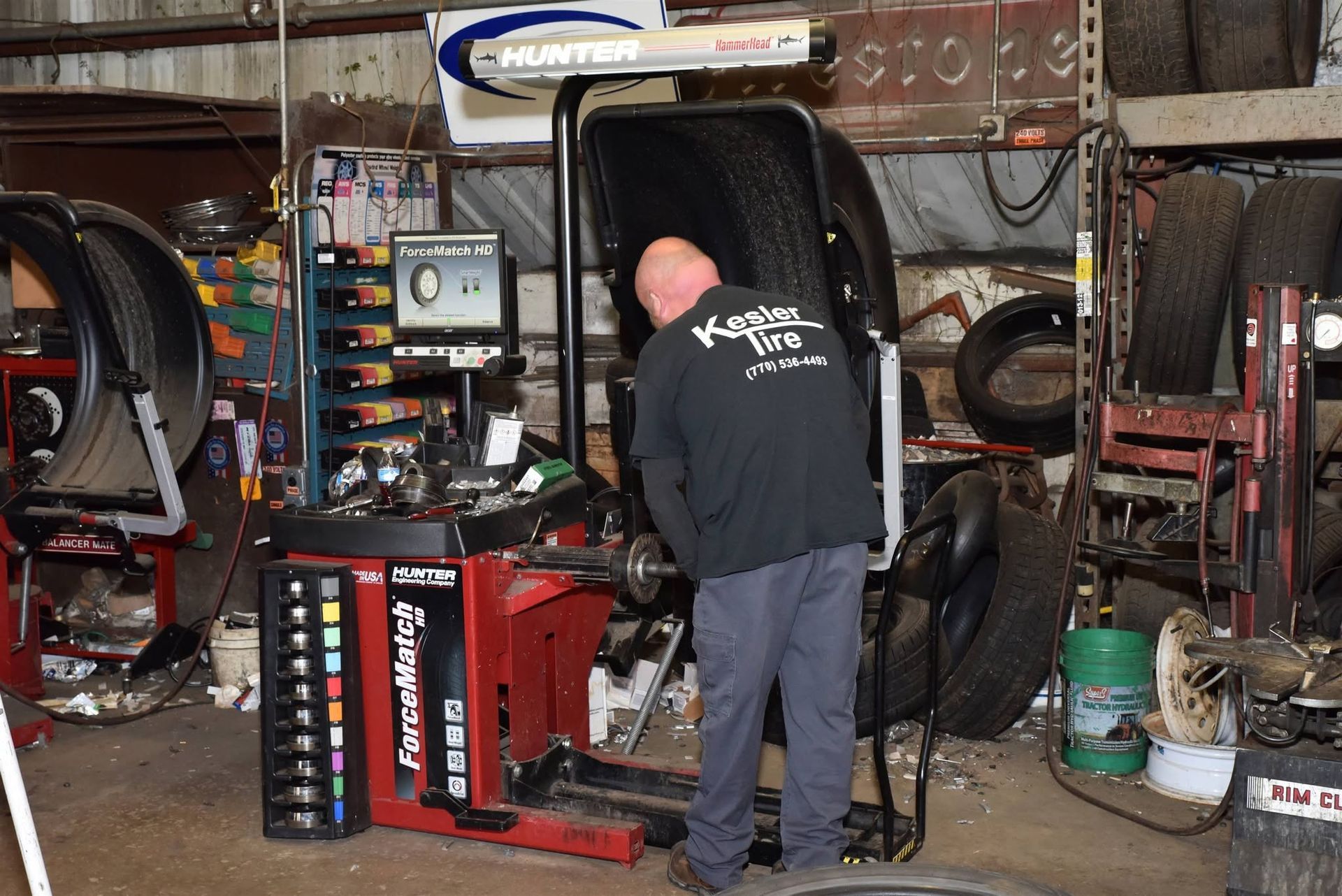 Mechanic stands in a cluttered auto shop, working on a red car door mounted upright.