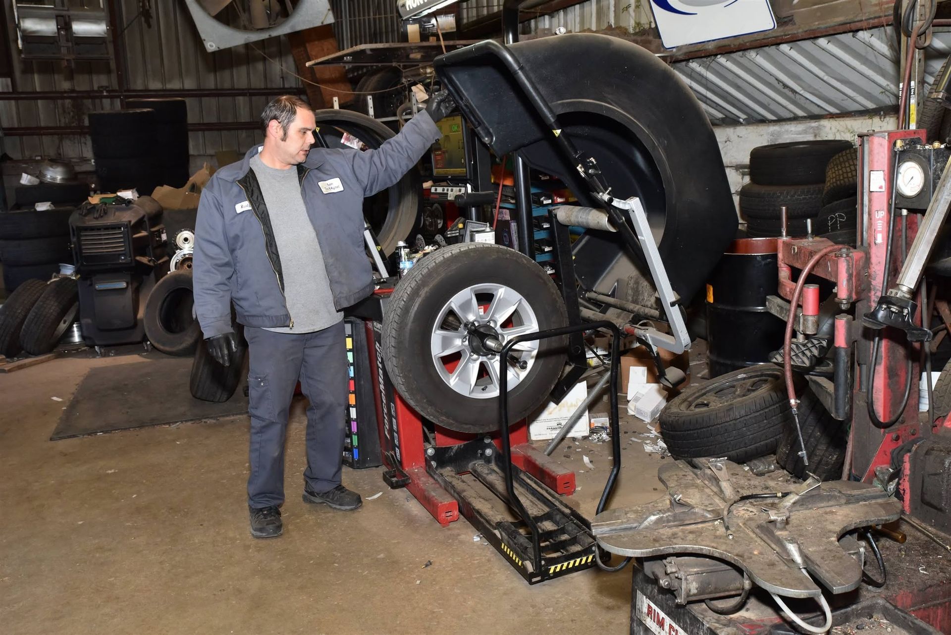 Mechanic standing beside a raised car in a tire shop, with tools and equipment around him