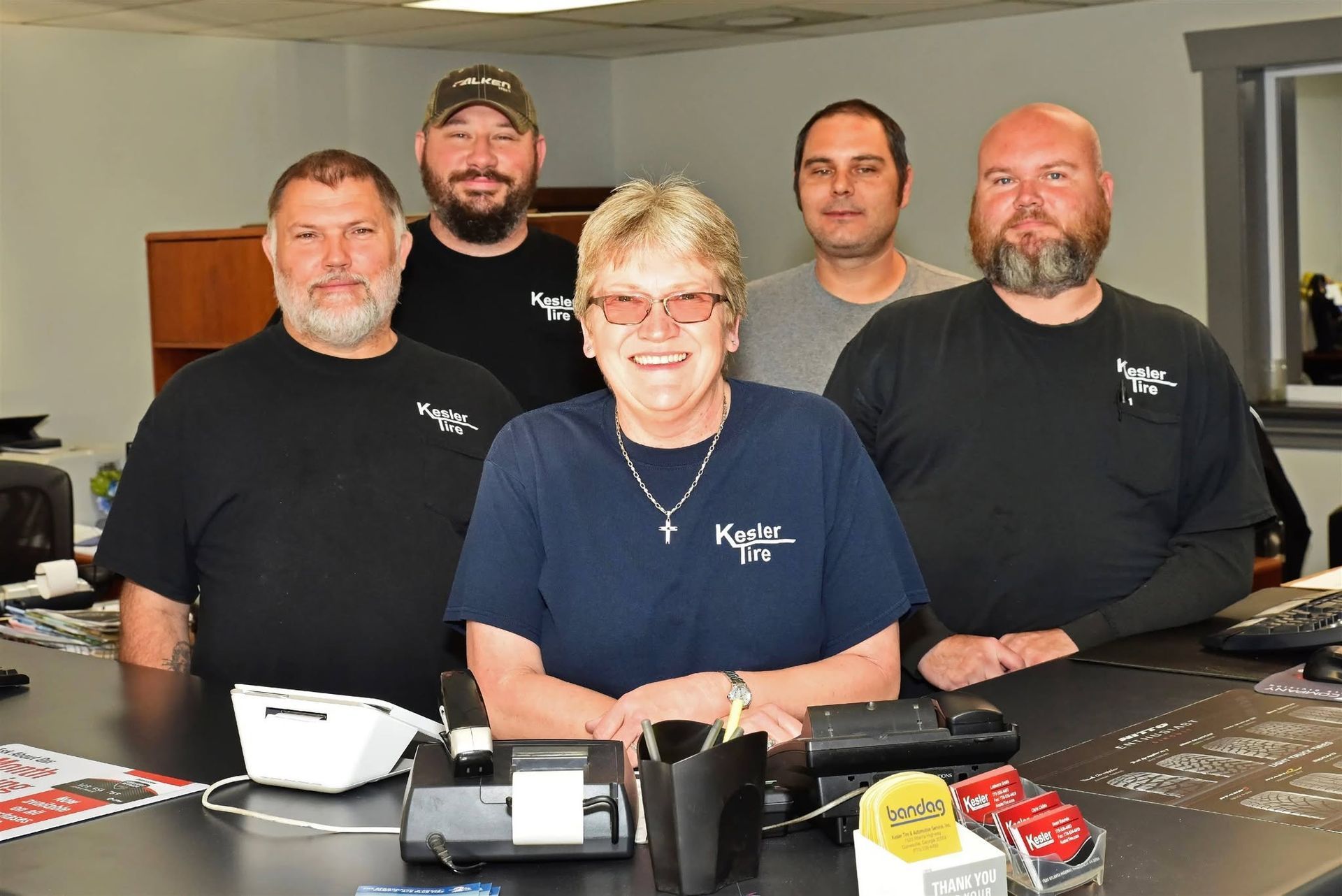 Five people in black shirts standing behind a counter in a shop, smiling at the camera