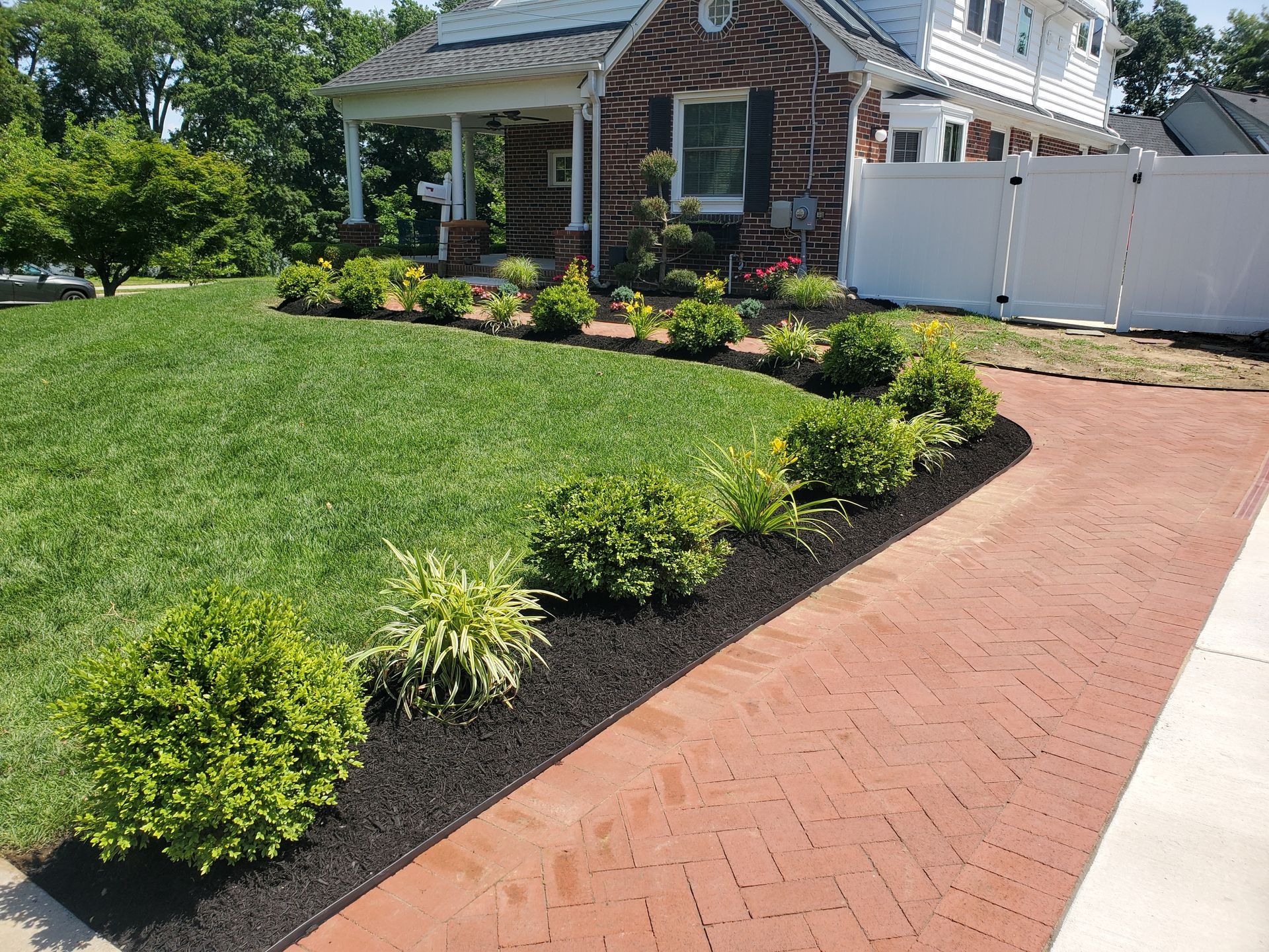 A brick driveway leading to a brick house with a white fence.