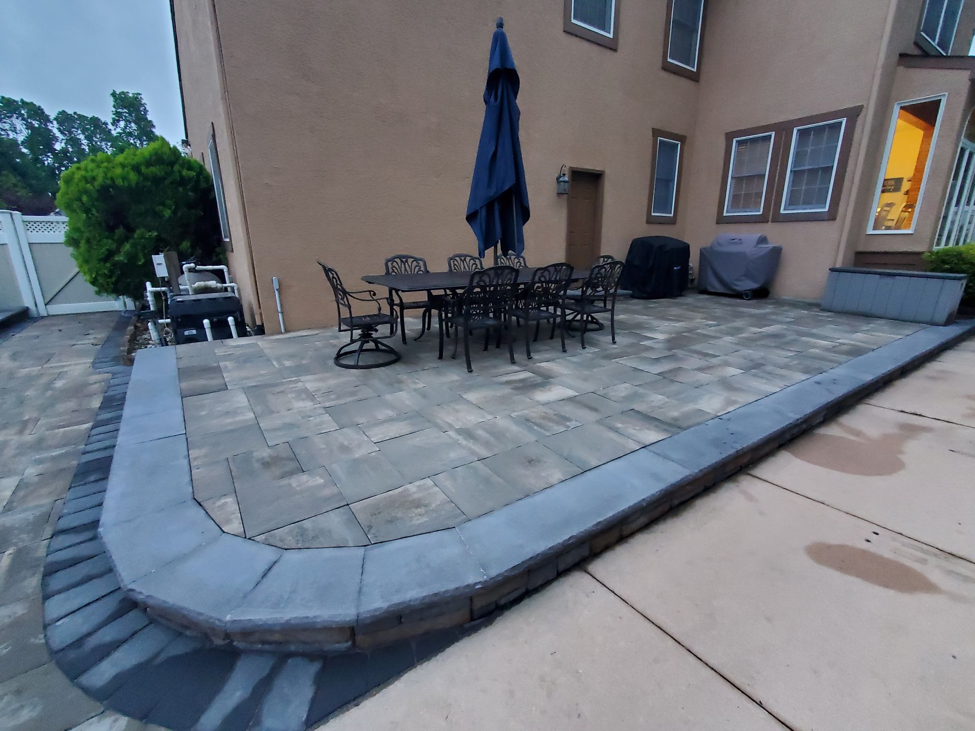 A patio with a table and chairs and an umbrella in front of a house.