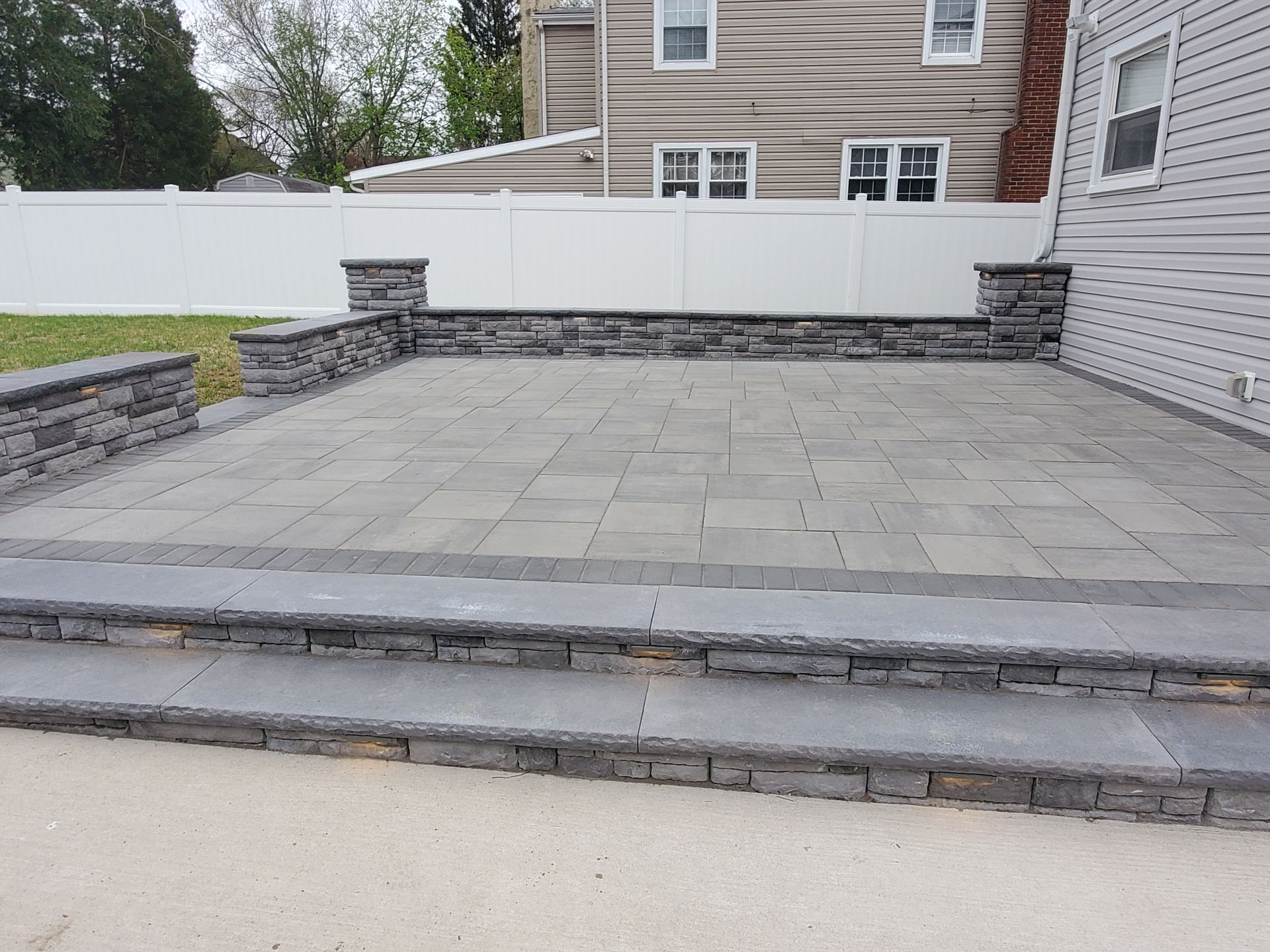 A patio with stairs and a white fence in front of a house.