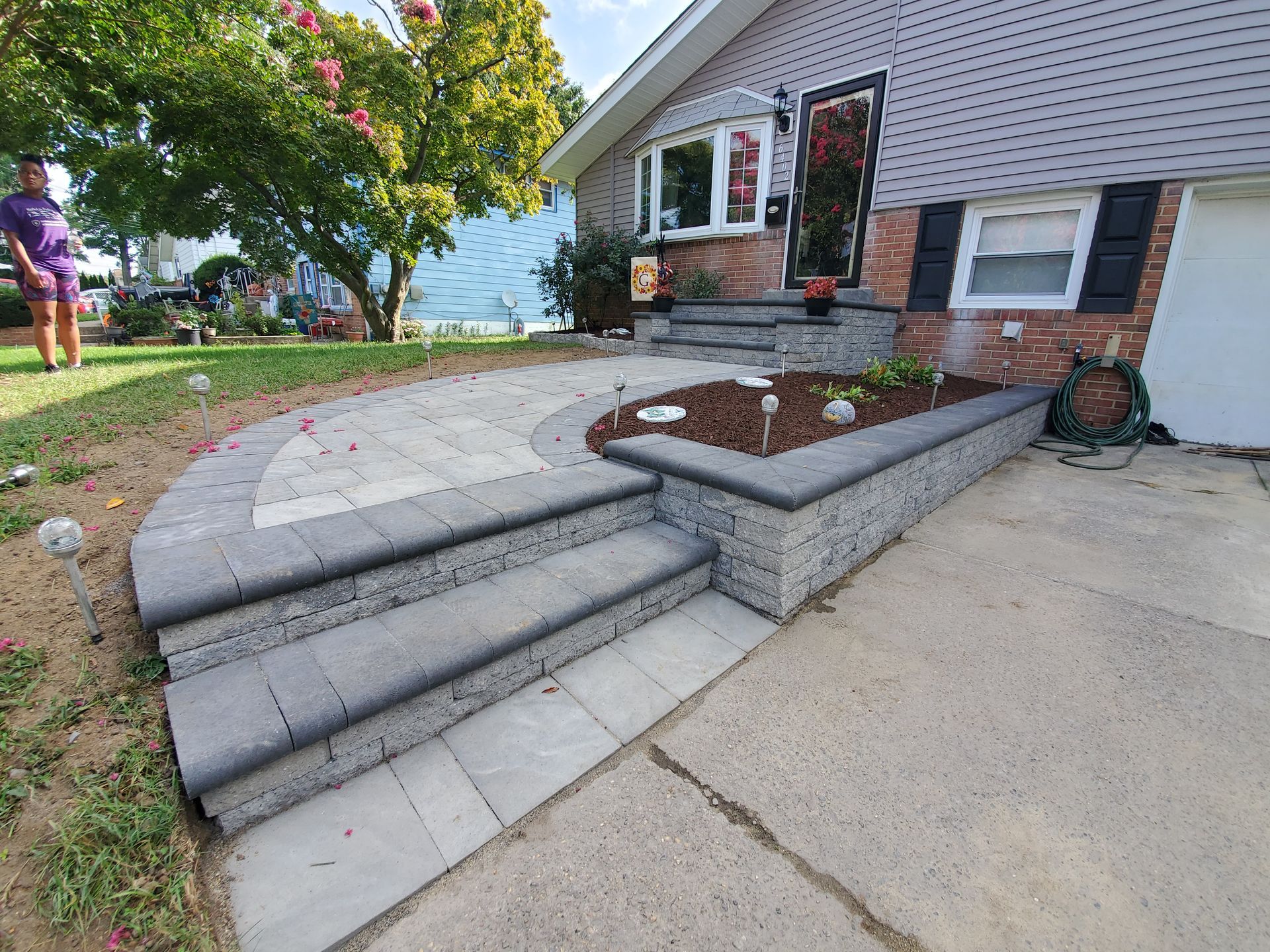A woman is standing in front of a house with stairs and a planter.
