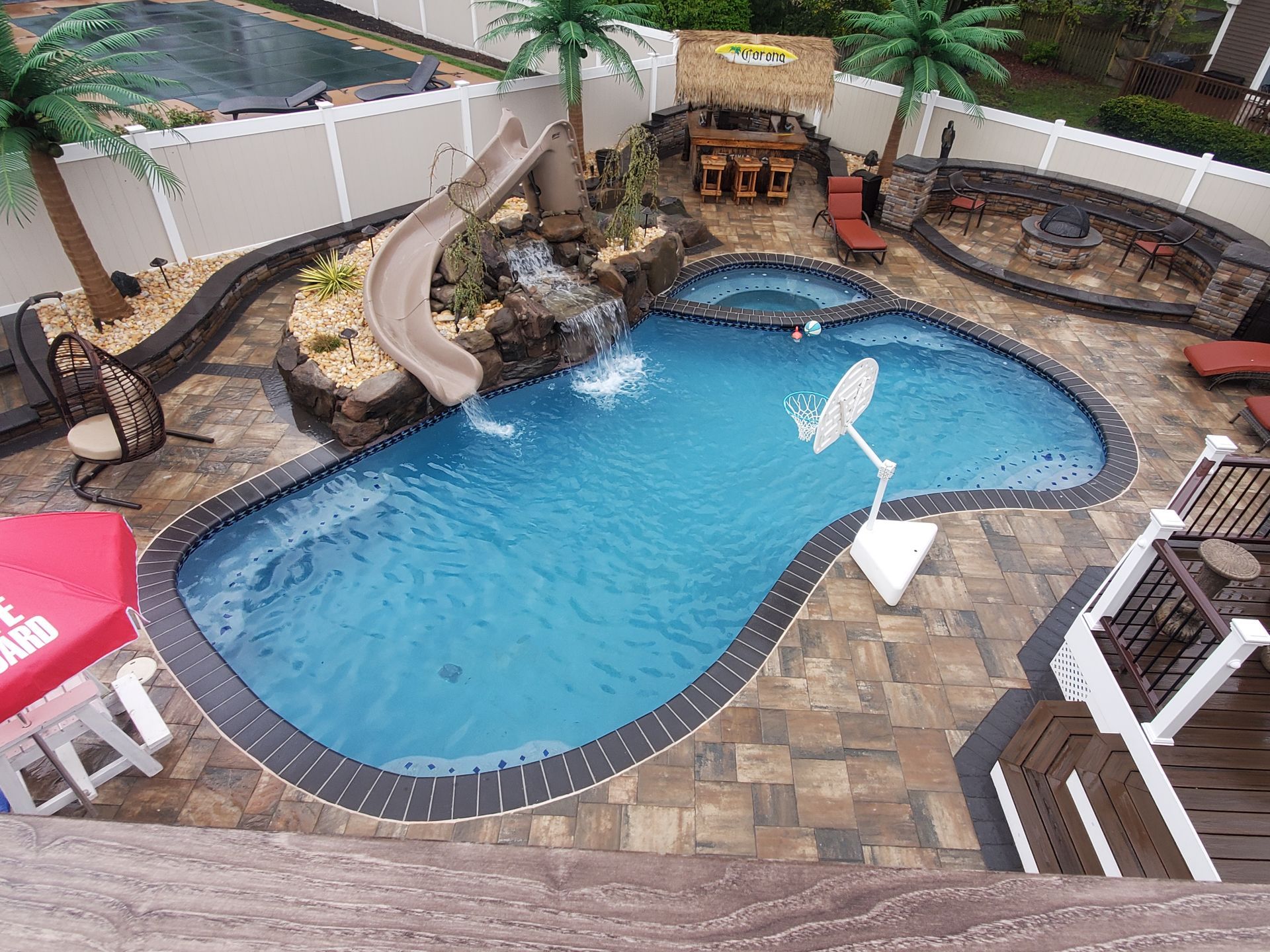 An aerial view of a large swimming pool with a slide and a basketball hoop.