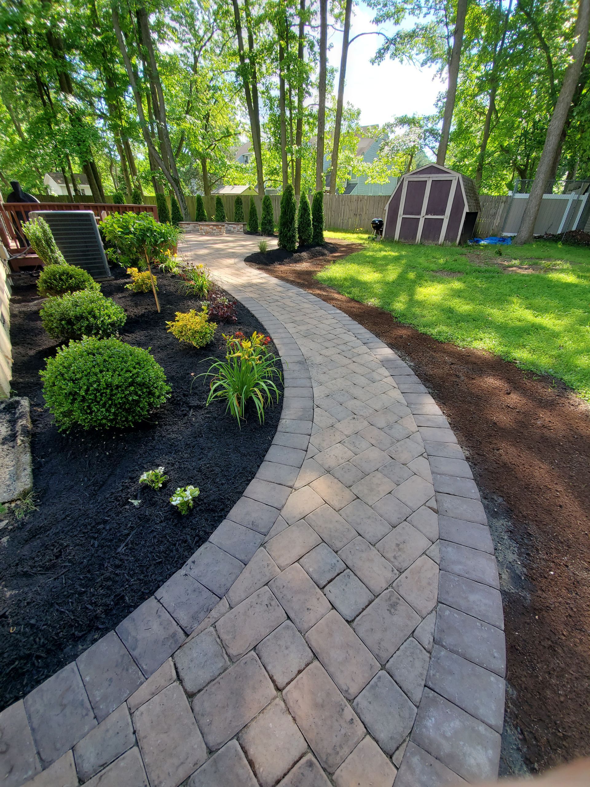 A brick walkway in a backyard surrounded by trees and bushes.