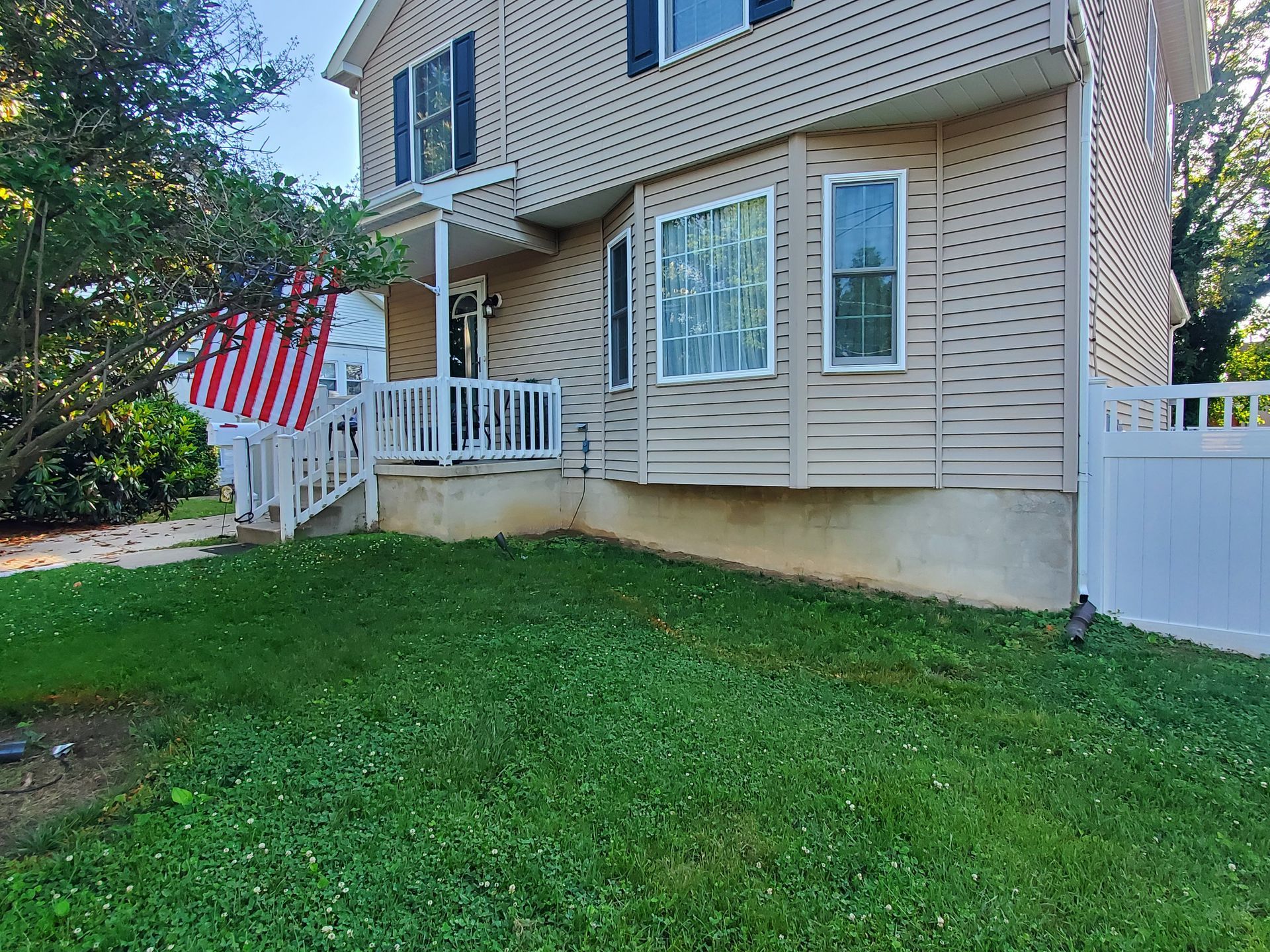 A house with a large lawn in front of it and an american flag on the porch.
