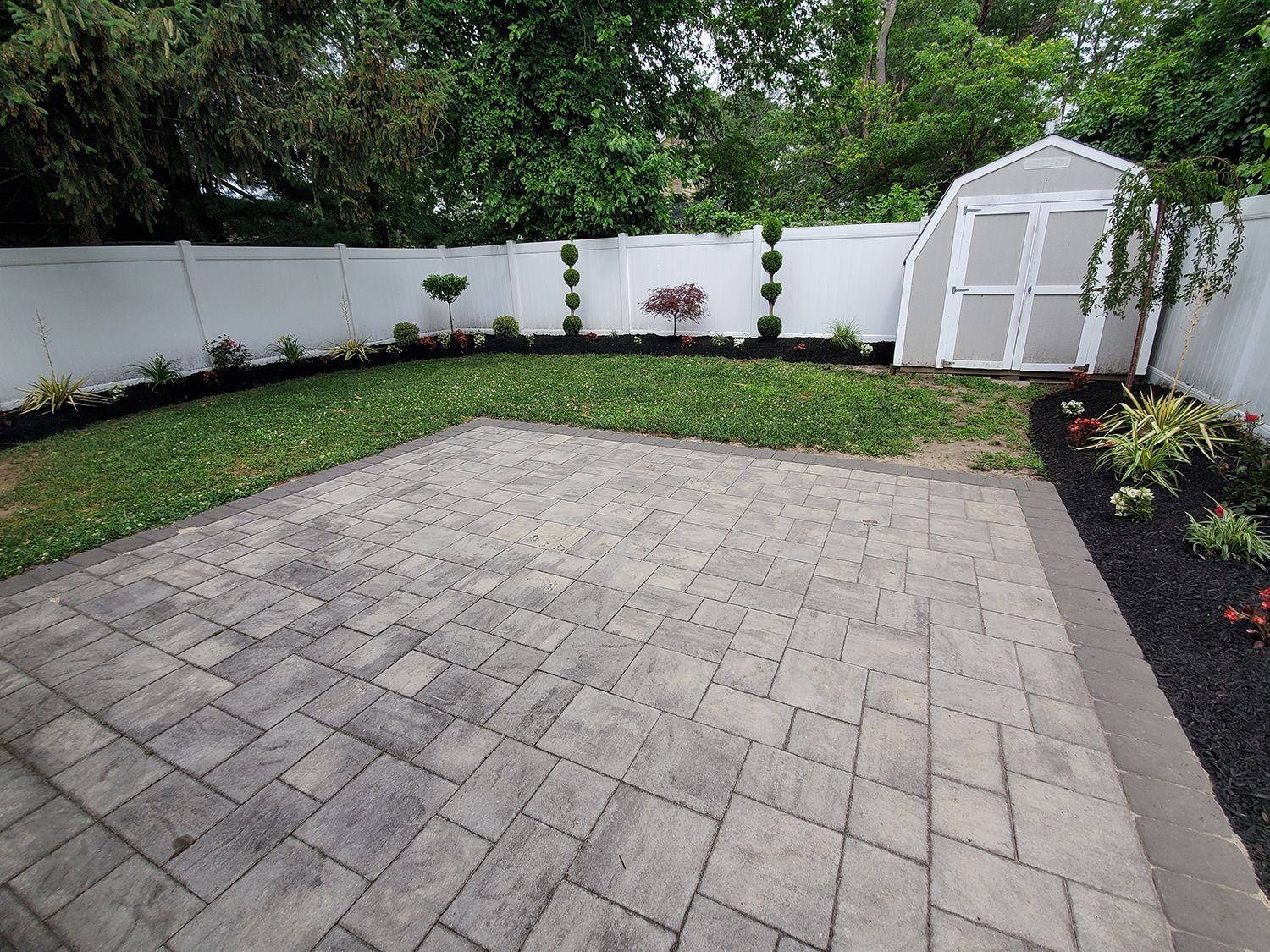 A backyard with a patio and a greenhouse in the background.