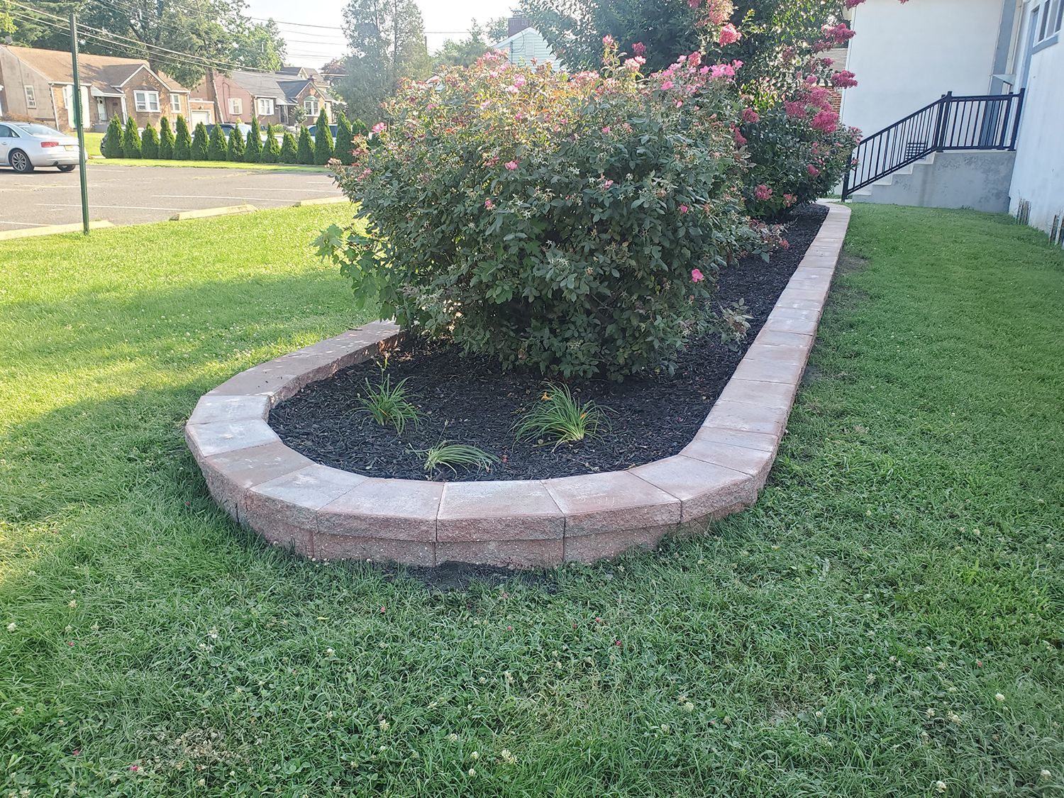 A brick planter with a bush in it is in the middle of a lush green lawn.