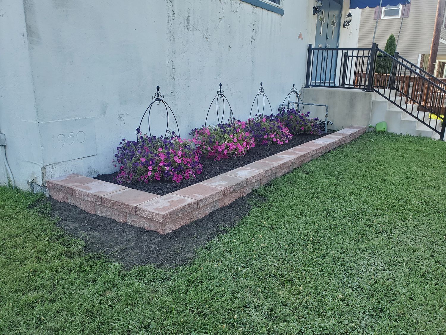A brick planter with pink flowers in front of a house.
