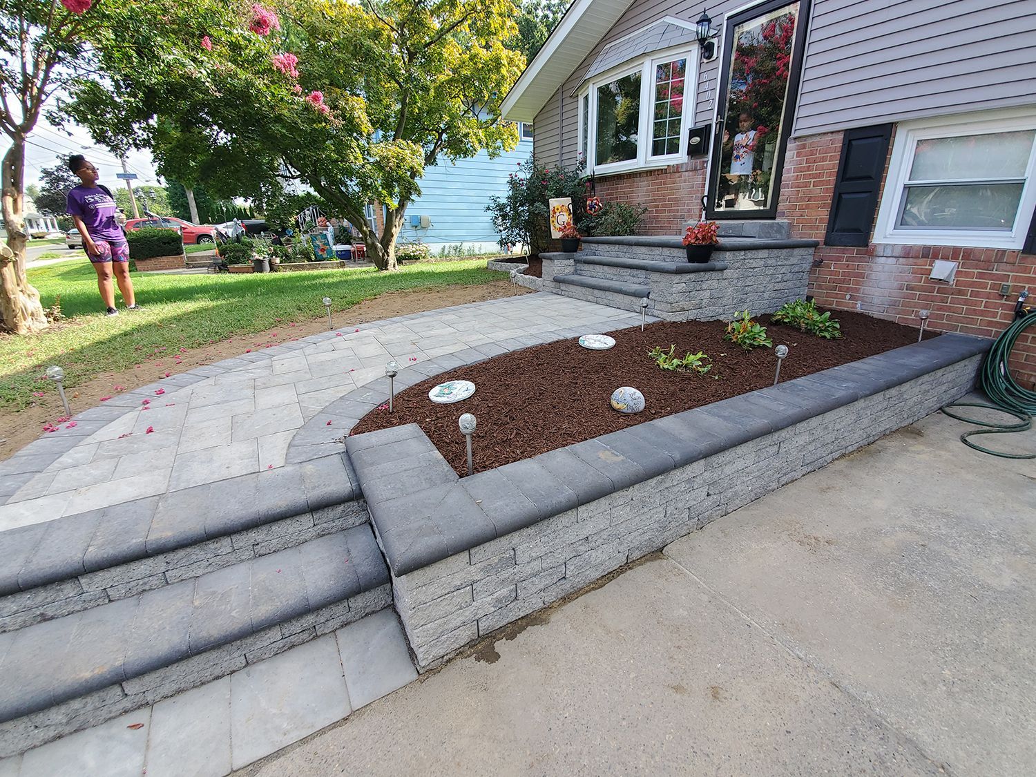 A woman is standing in front of a house with a garden in front of it.