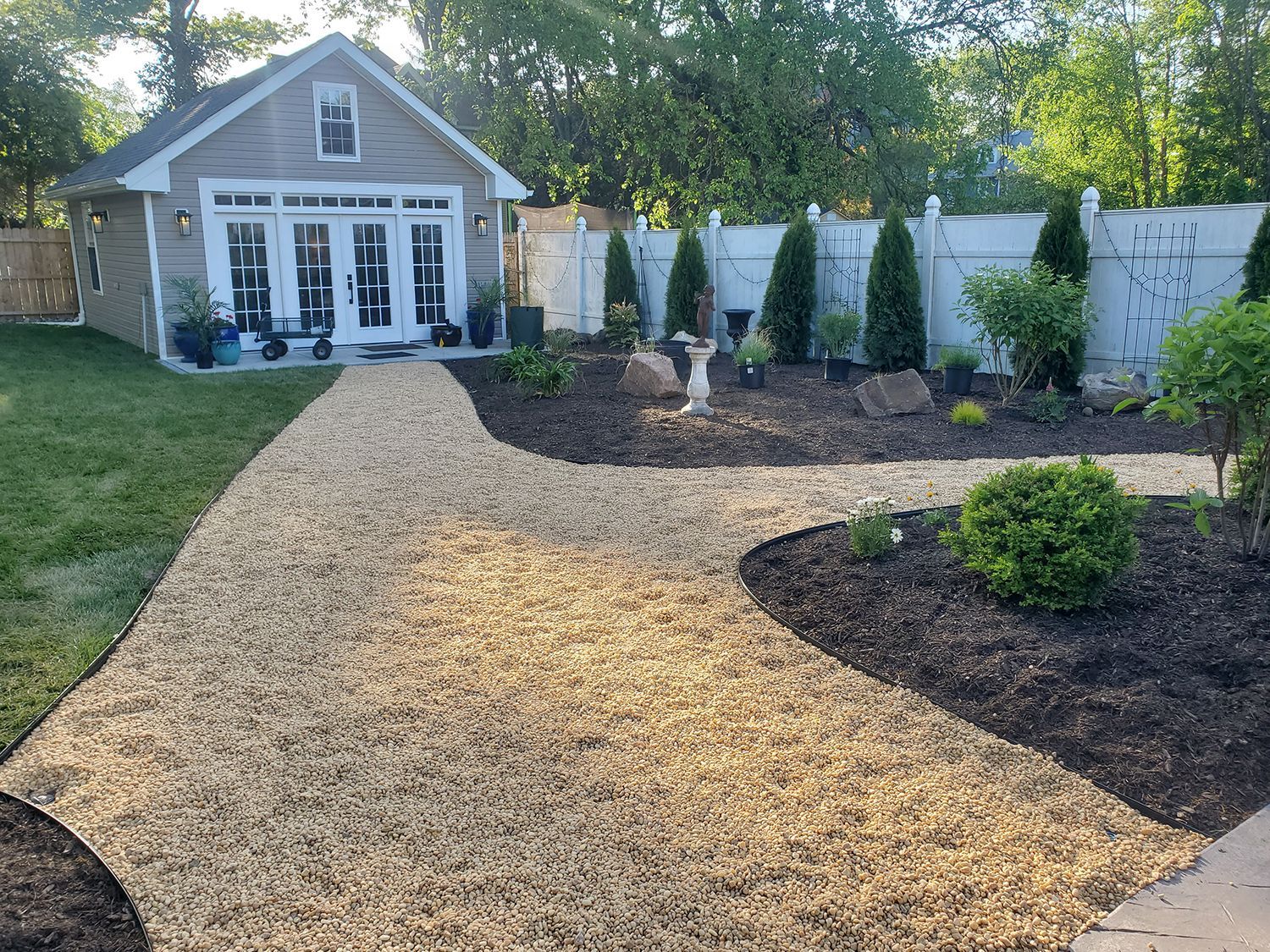 A gravel path leading to a small house with a white fence.