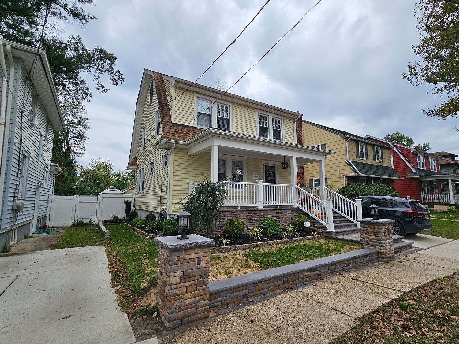 A large yellow house with a white porch and a car parked in front of it.